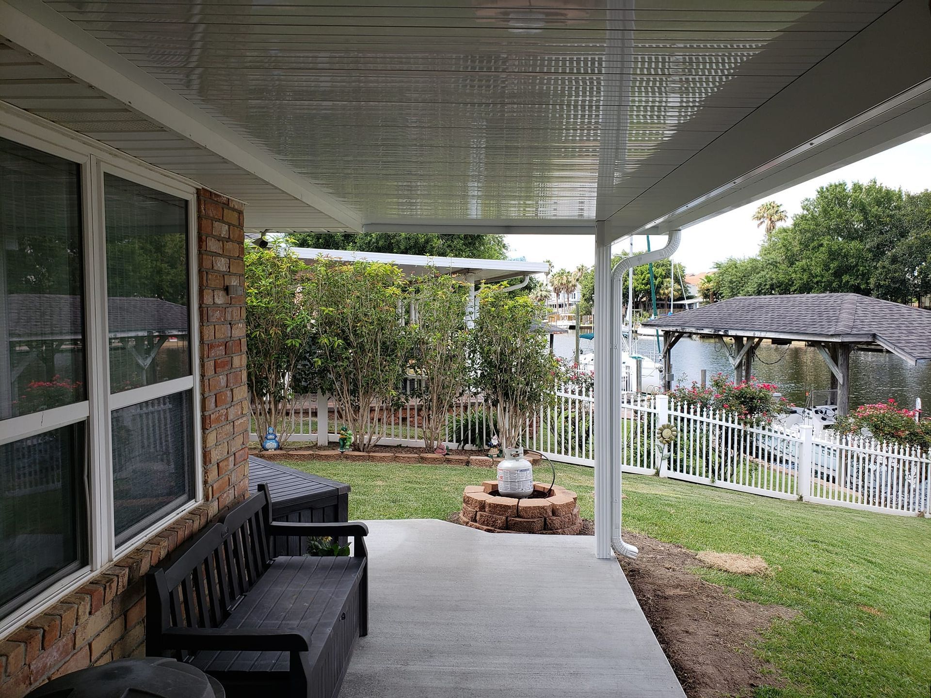 Covered patio with bench, view of yard with white fence and trees.