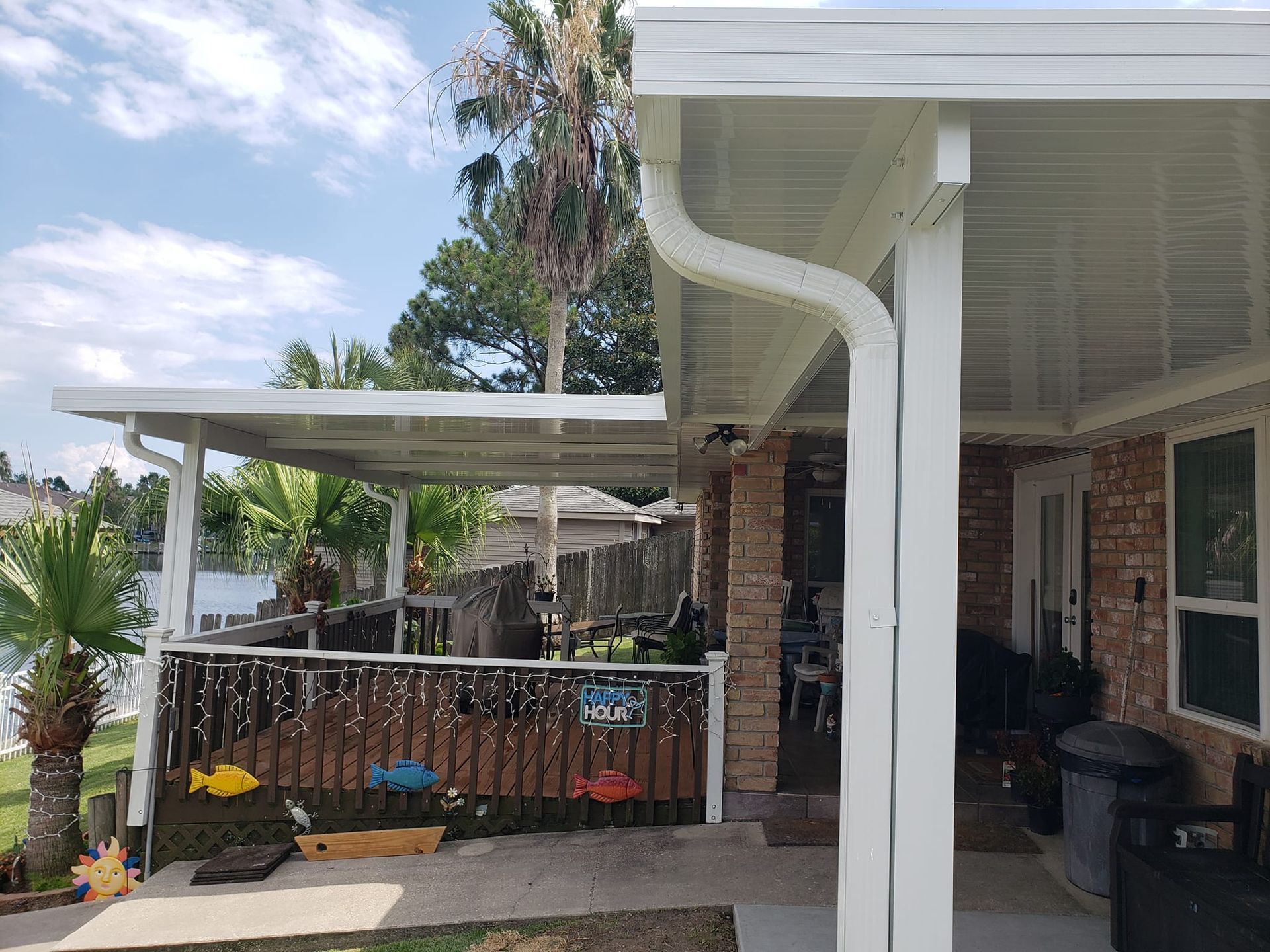 White patio cover attached to a brick house, overlooking a lake.