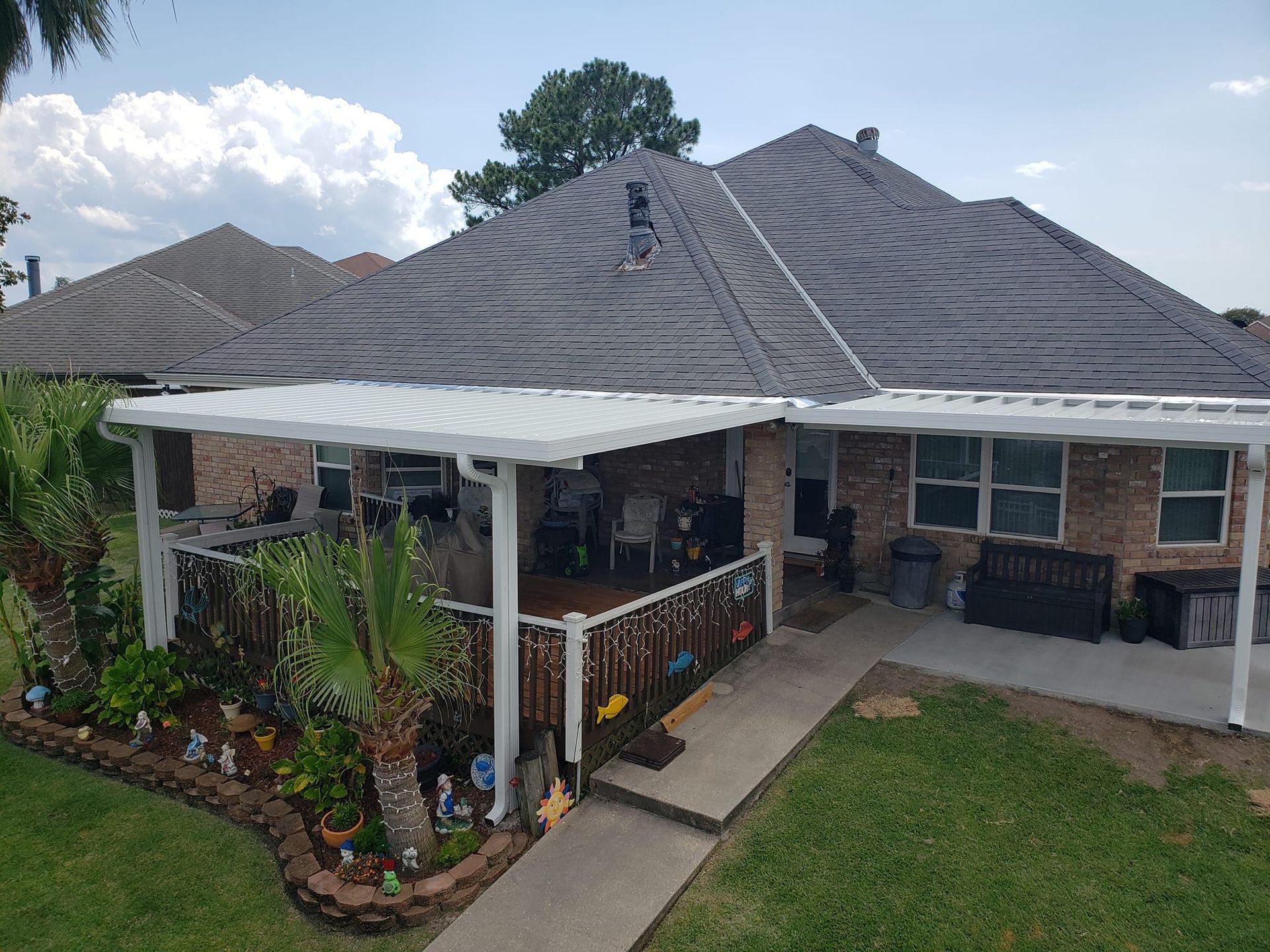 A house with a patio, gray roof, green lawn, and small garden with decorative objects.