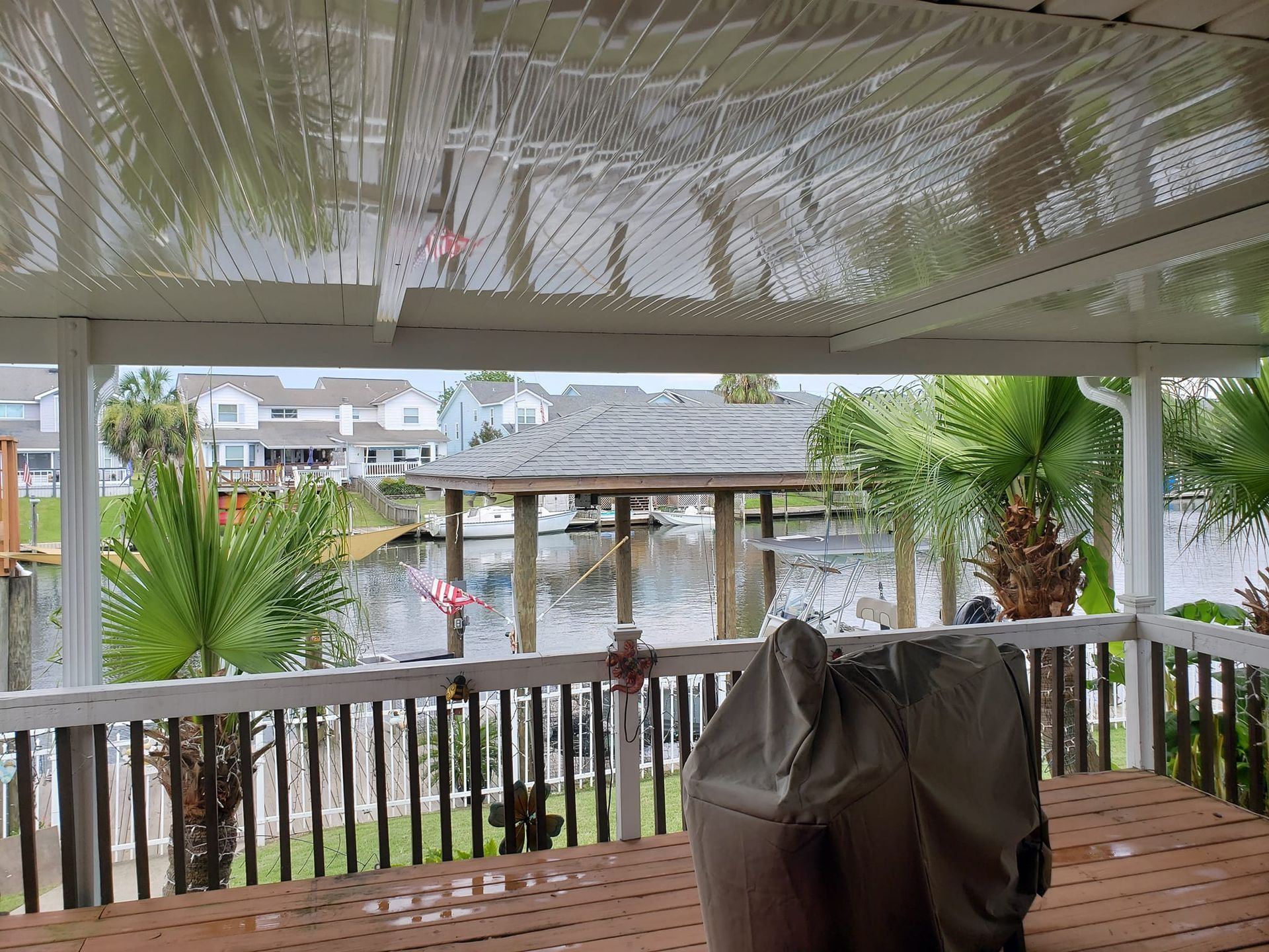 Covered patio overlooking a canal and dock, with palm trees and a grill covered.
