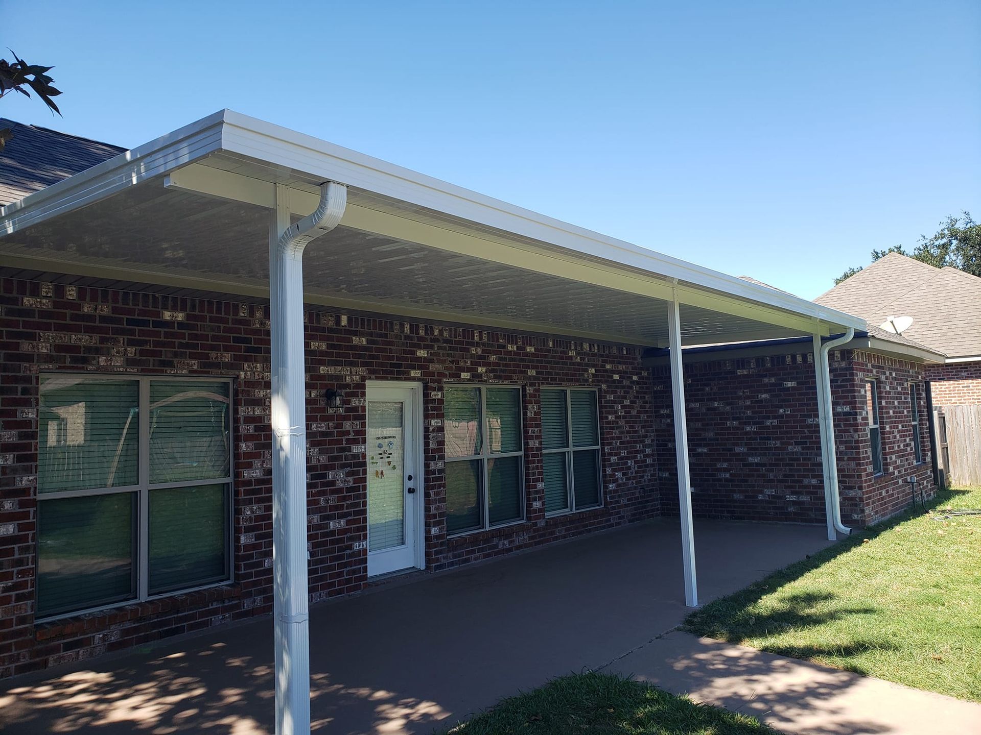 A brick house with a white covered patio, supported by white posts on a sunny day.