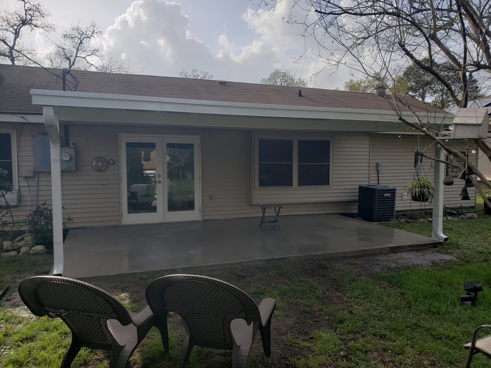 Backyard patio with two chairs, French doors, and a covered roof.