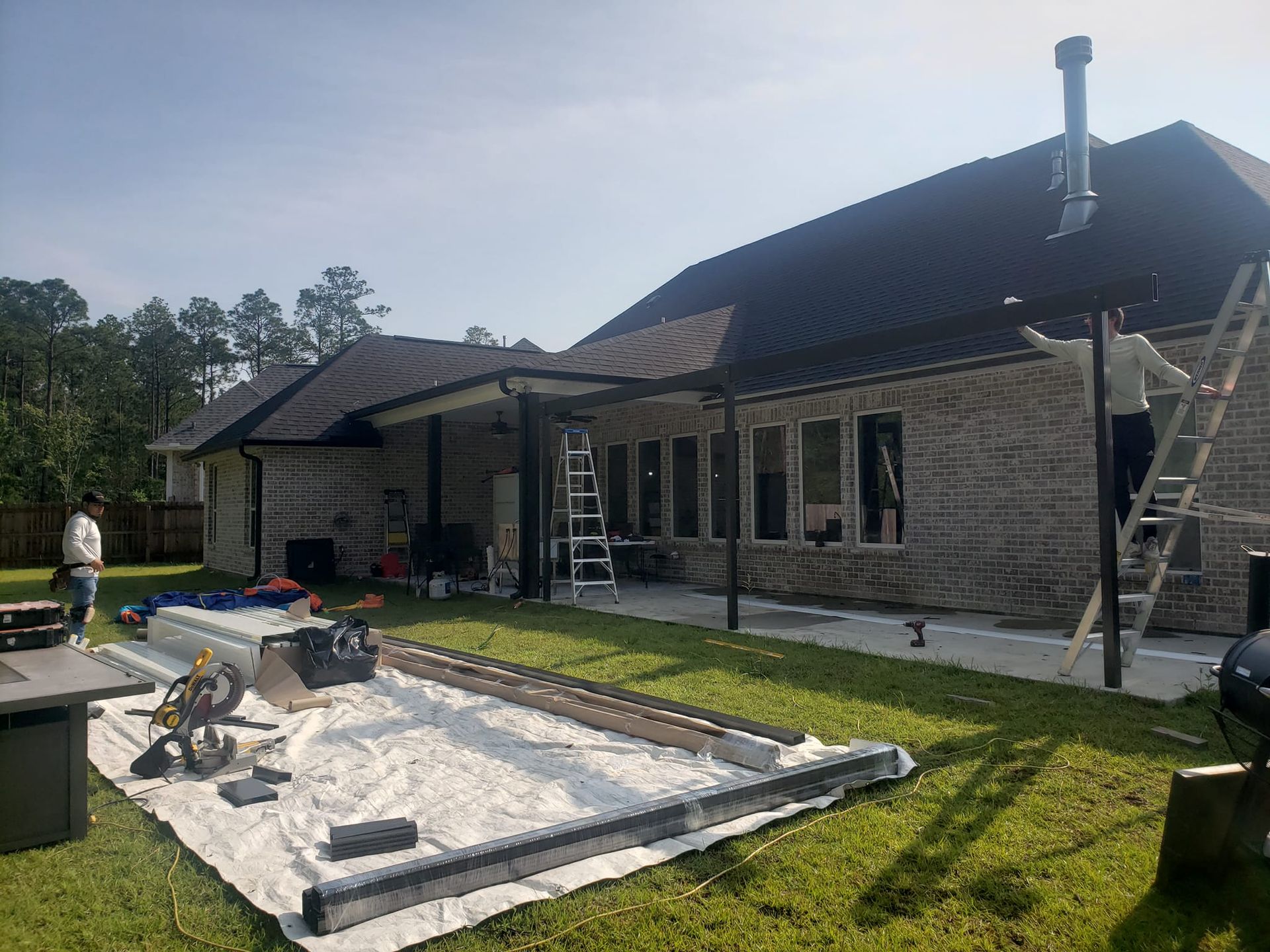 Construction workers building a patio cover next to a brick house on a sunny day.
