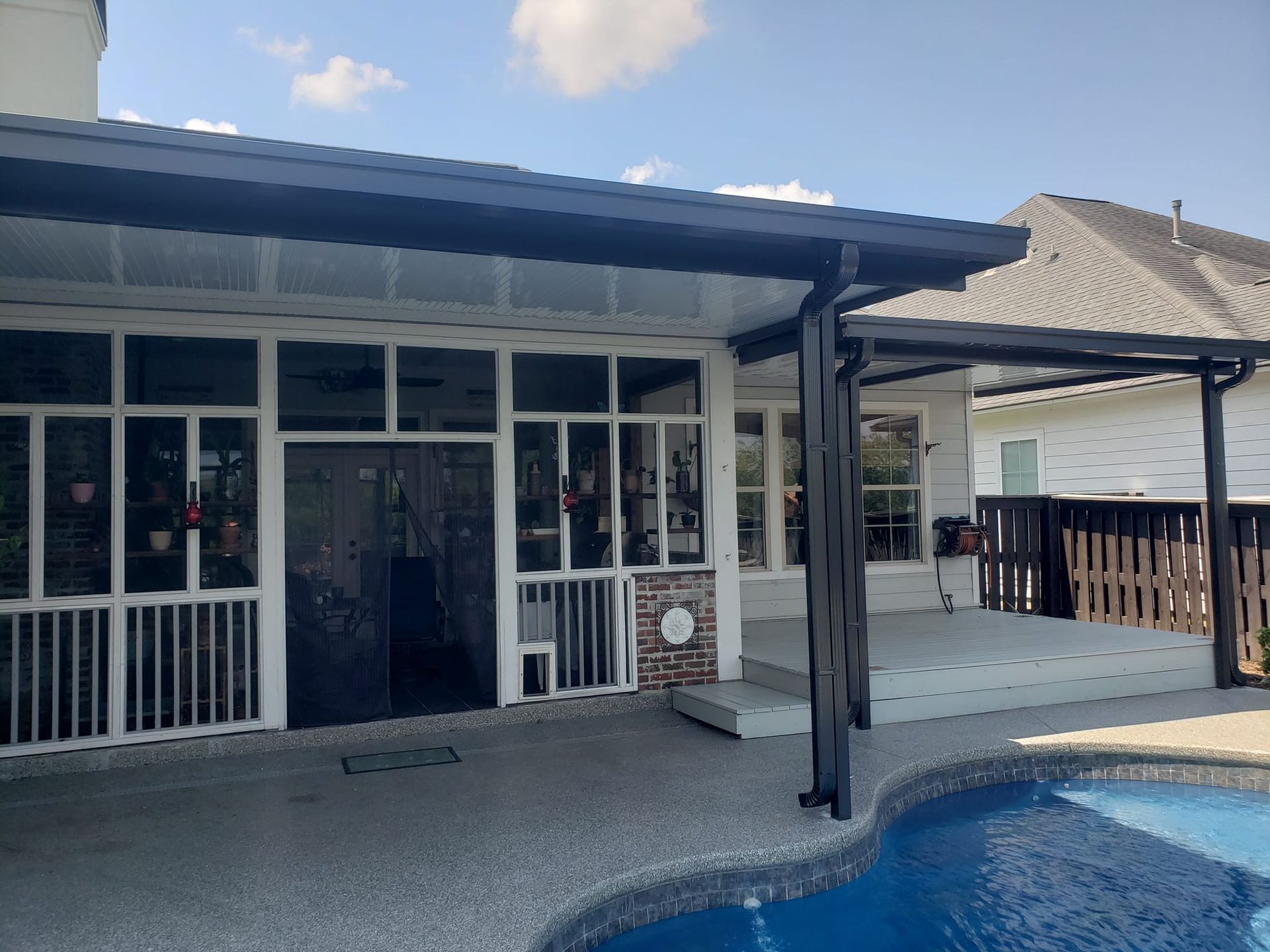 Screened-in porch with pool in foreground; gray deck and roof; white trim, black accents.