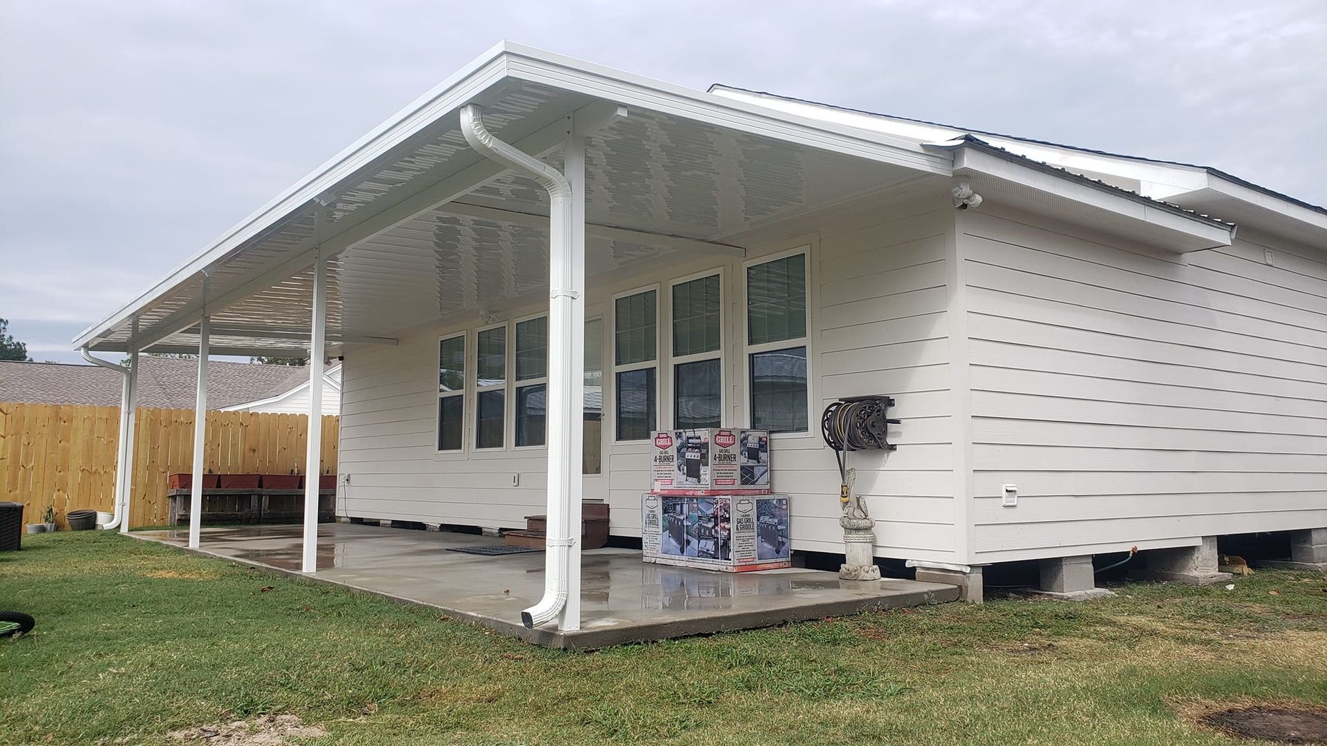 White house with a covered patio and white siding. Boxes sit on the patio; green grass in the foreground.