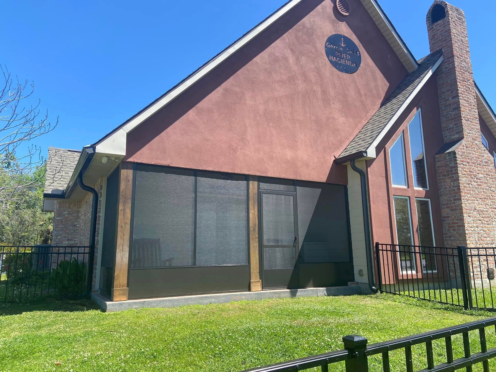 Screened porch with brown trim, a red stucco house, and a brick chimney on a sunny day.