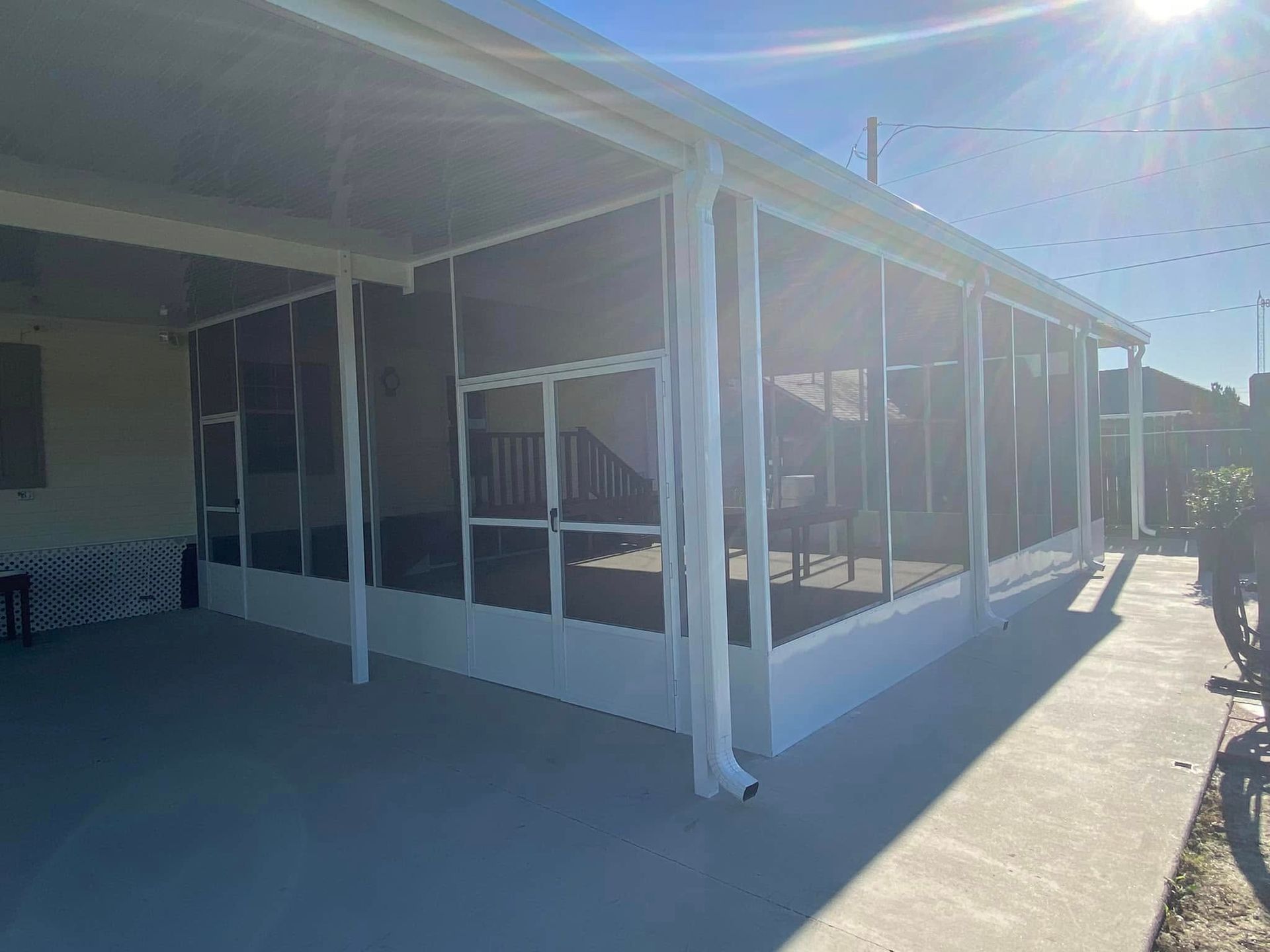 Screened-in porch with white frame, concrete floor, and sunlight.