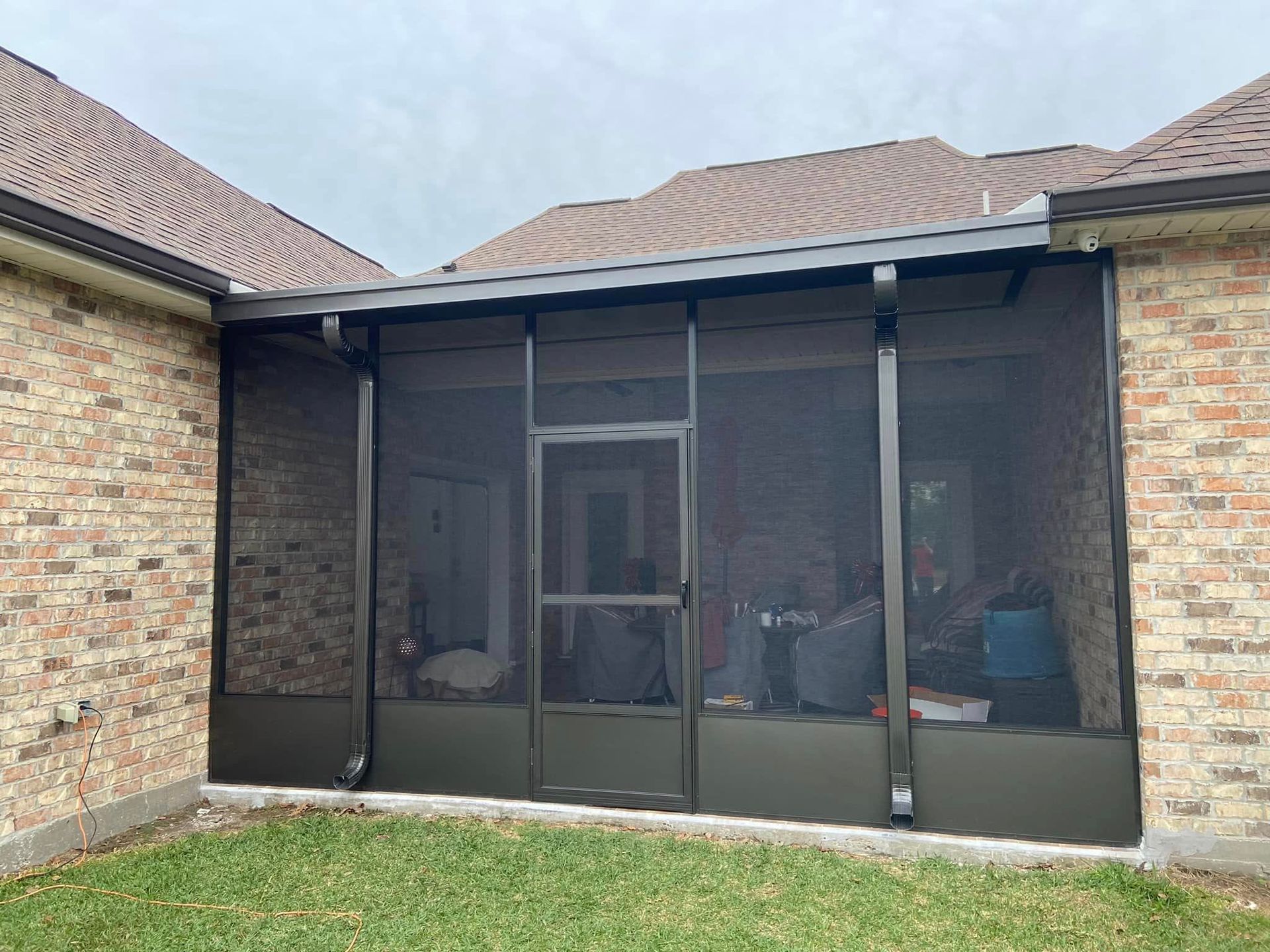 Screened porch with dark frame, brick exterior, and green lawn.