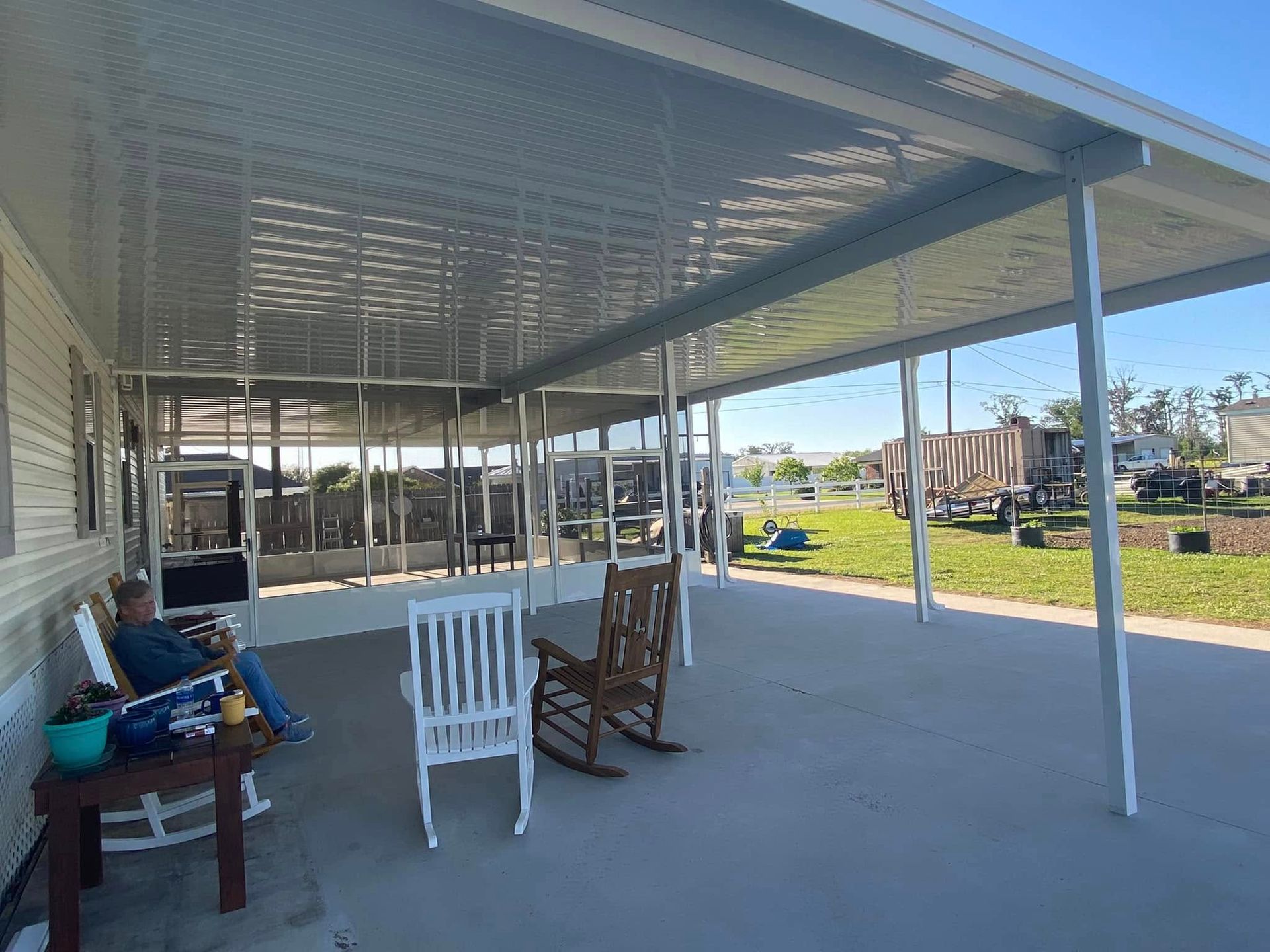 Covered patio with chairs, person seated. Sunny outdoor setting.
