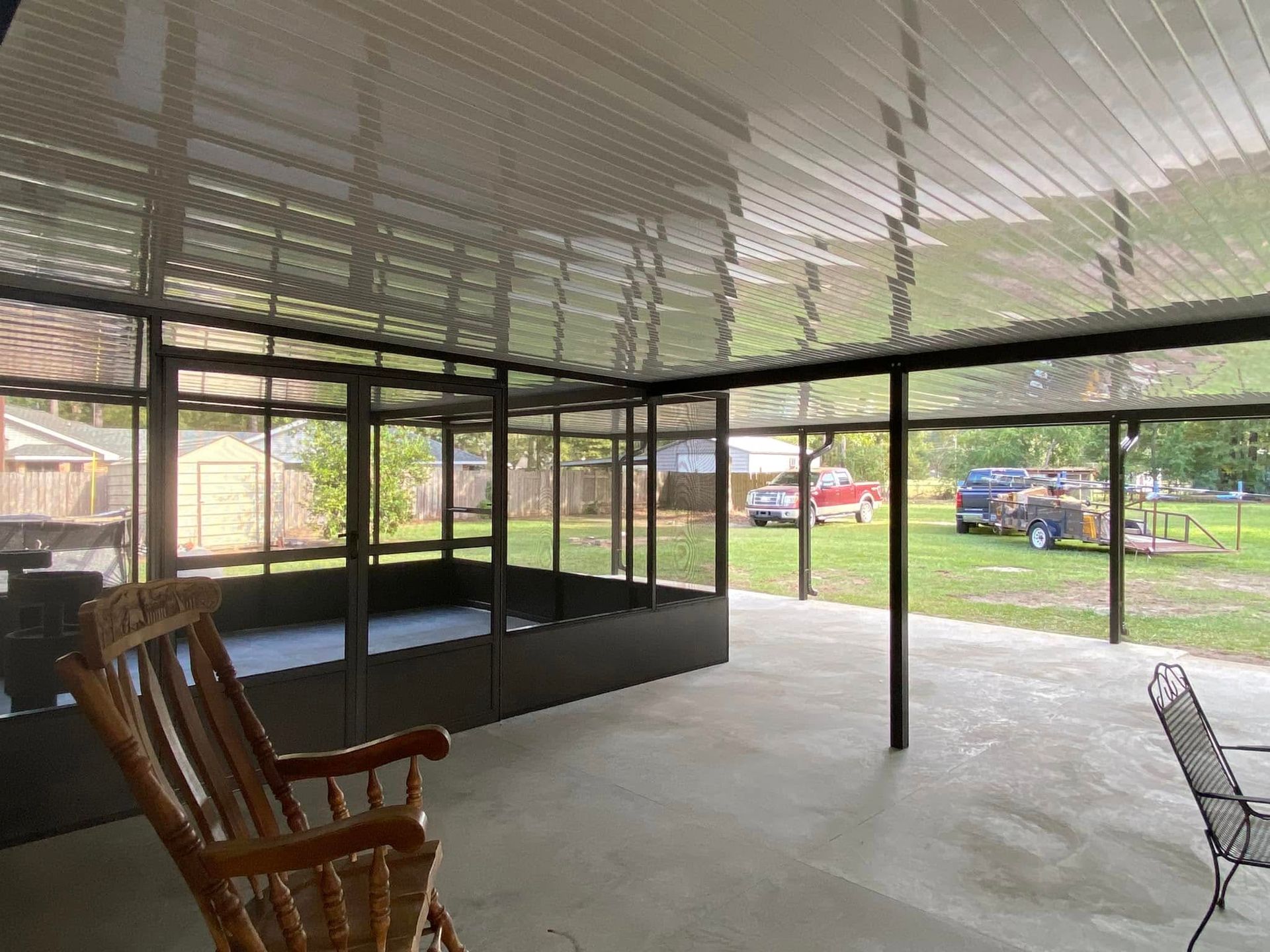 Screened-in patio with rocking chair, overlooking a yard with vehicles and a shed.