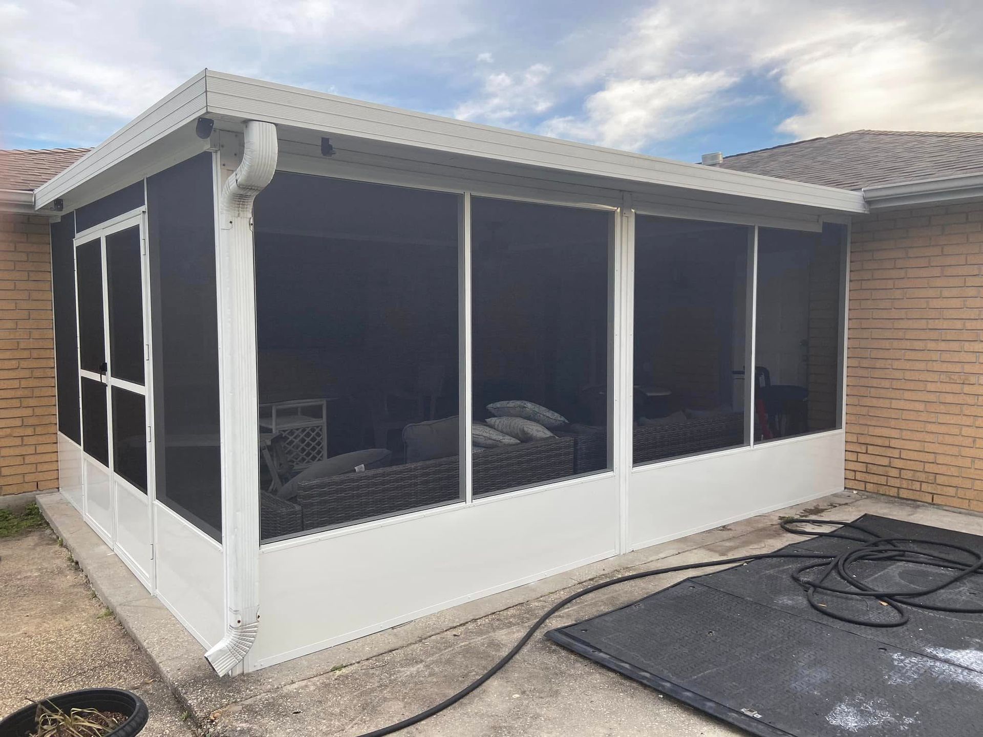 Screened-in patio attached to a brick house, white frame with dark screens, concrete floor.