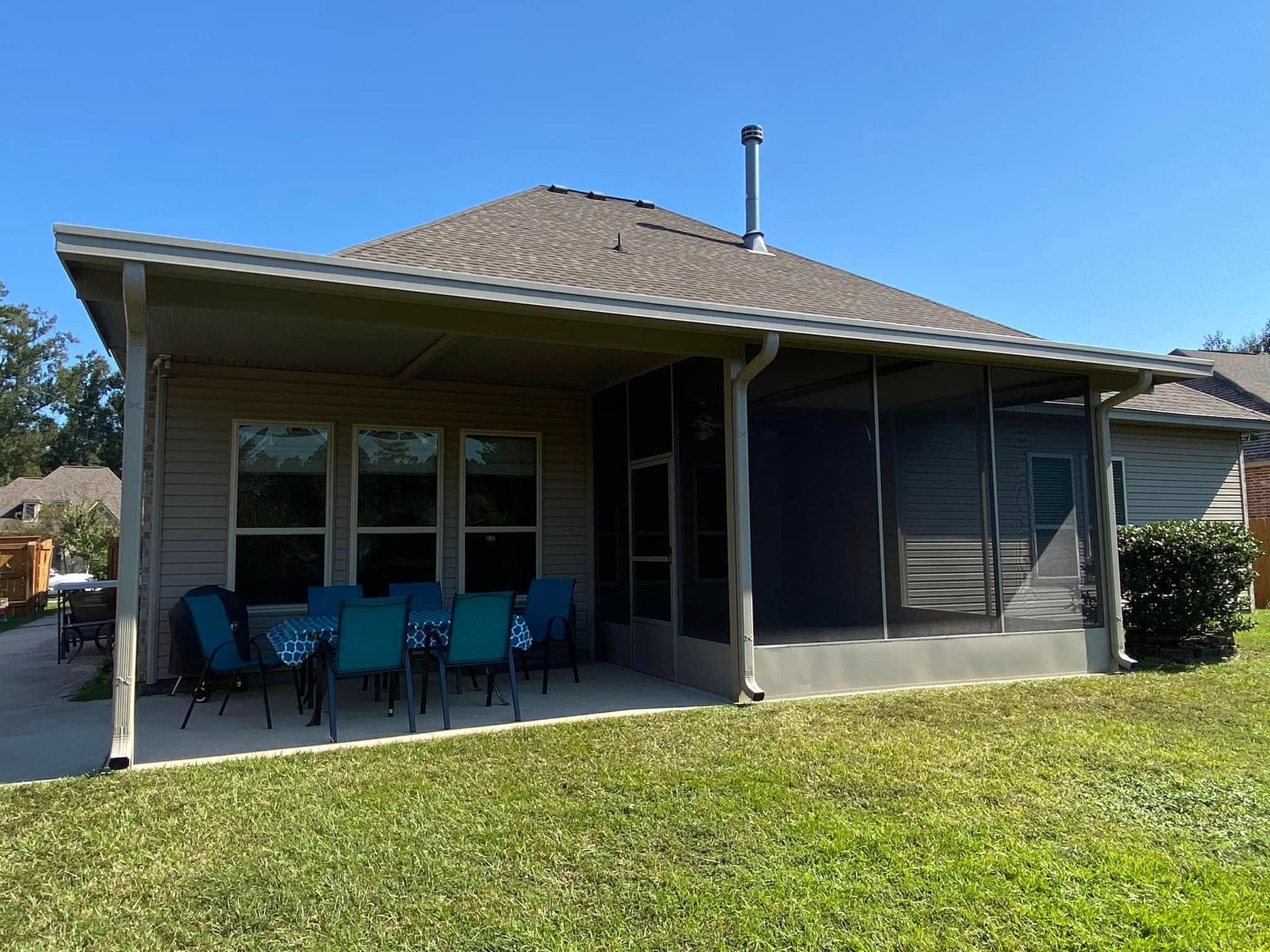 Backyard patio with blue chairs and screened-in porch under a sunny sky.