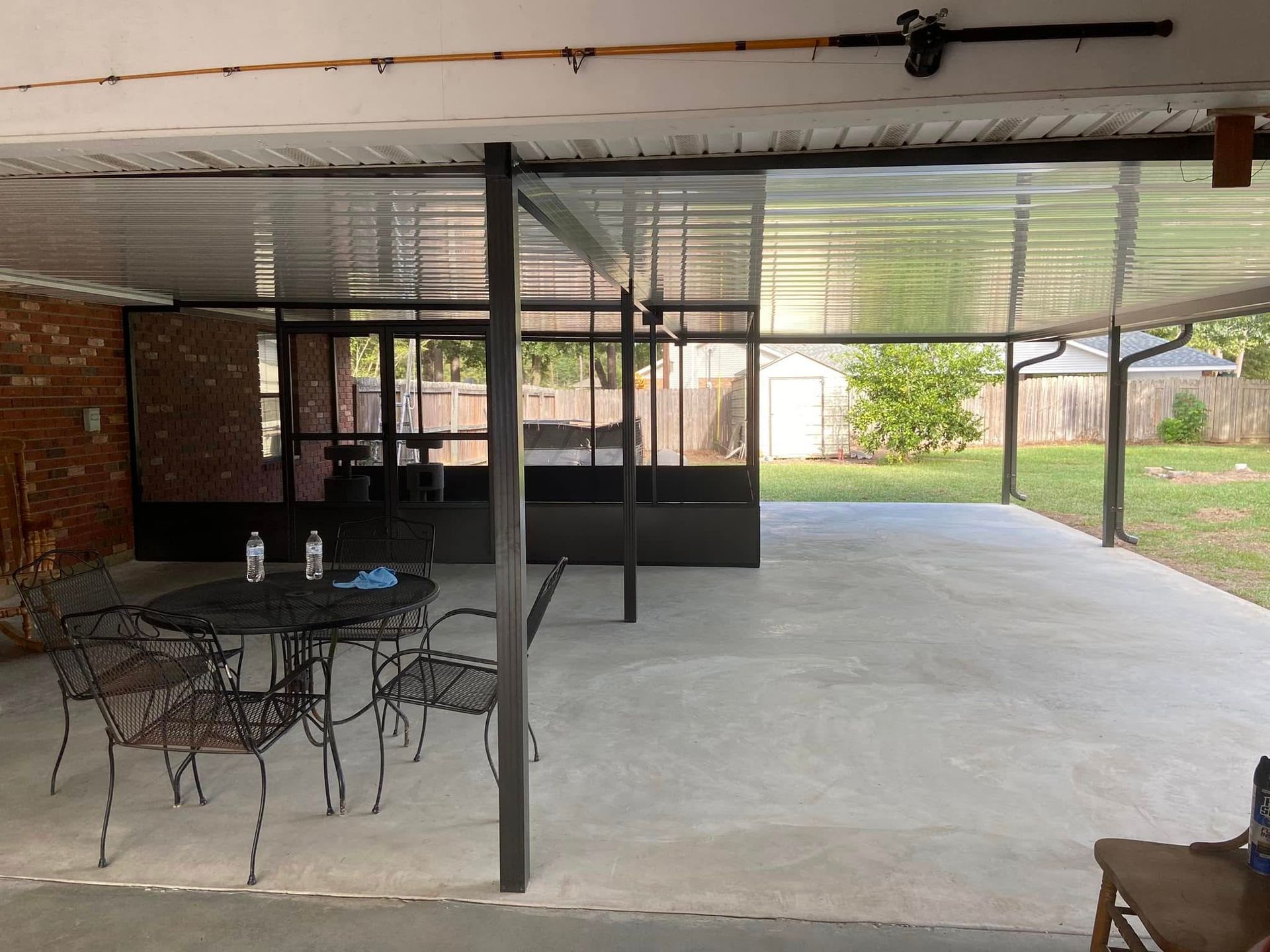 Covered patio with metal frame, concrete floor, black table and chairs, and backyard view.