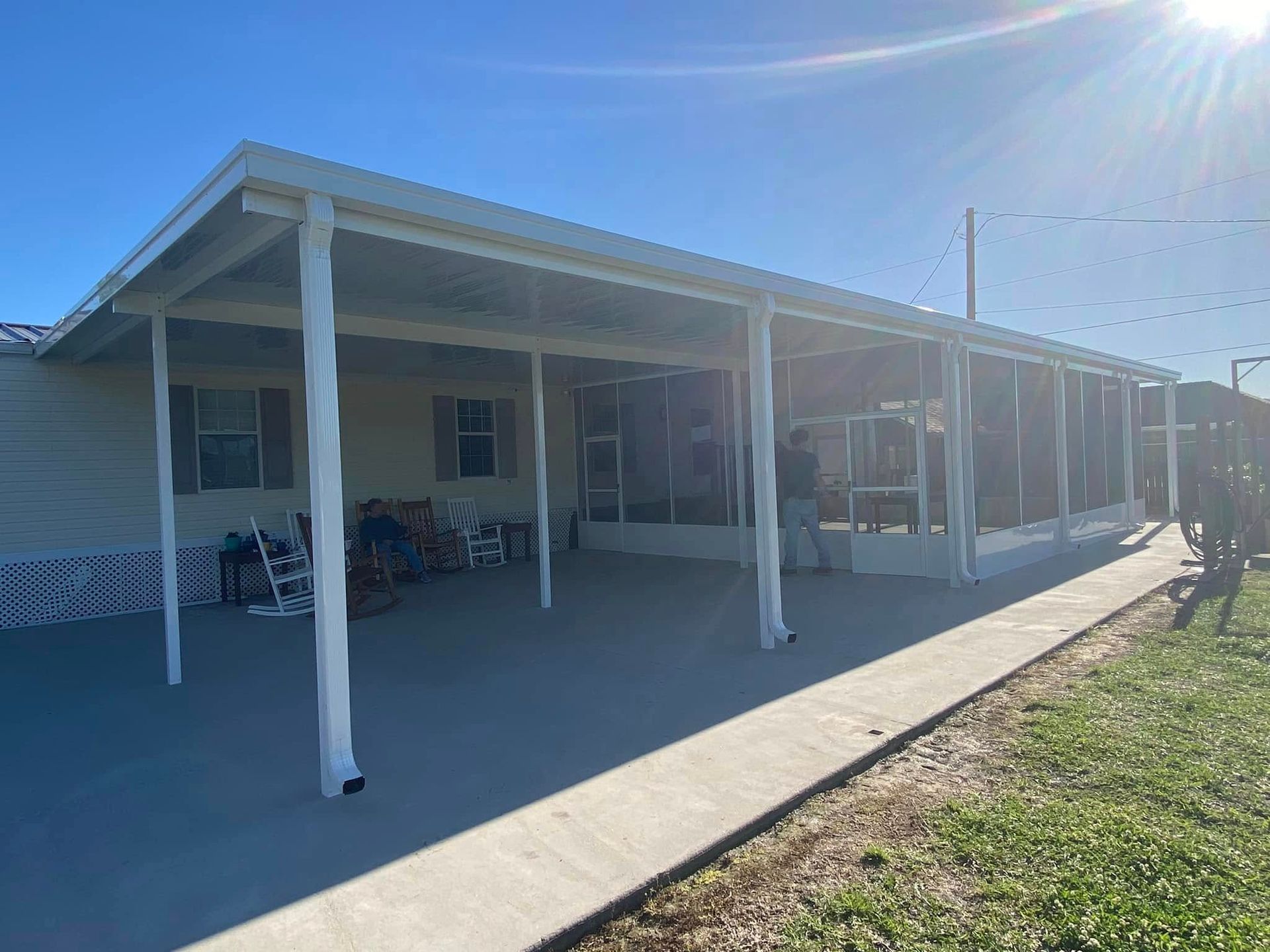A home with a white covered porch and screened-in area; sunlight casts shadows on the concrete.
