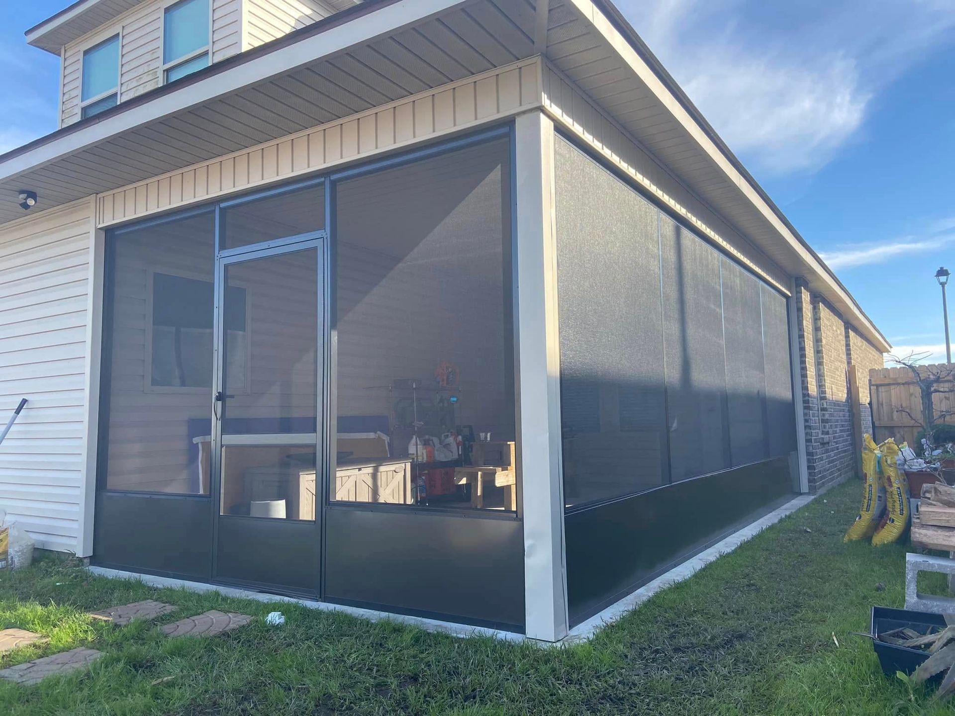 Screened-in porch attached to a house; black screens, dark trim, white siding. Green grass, sunny day.