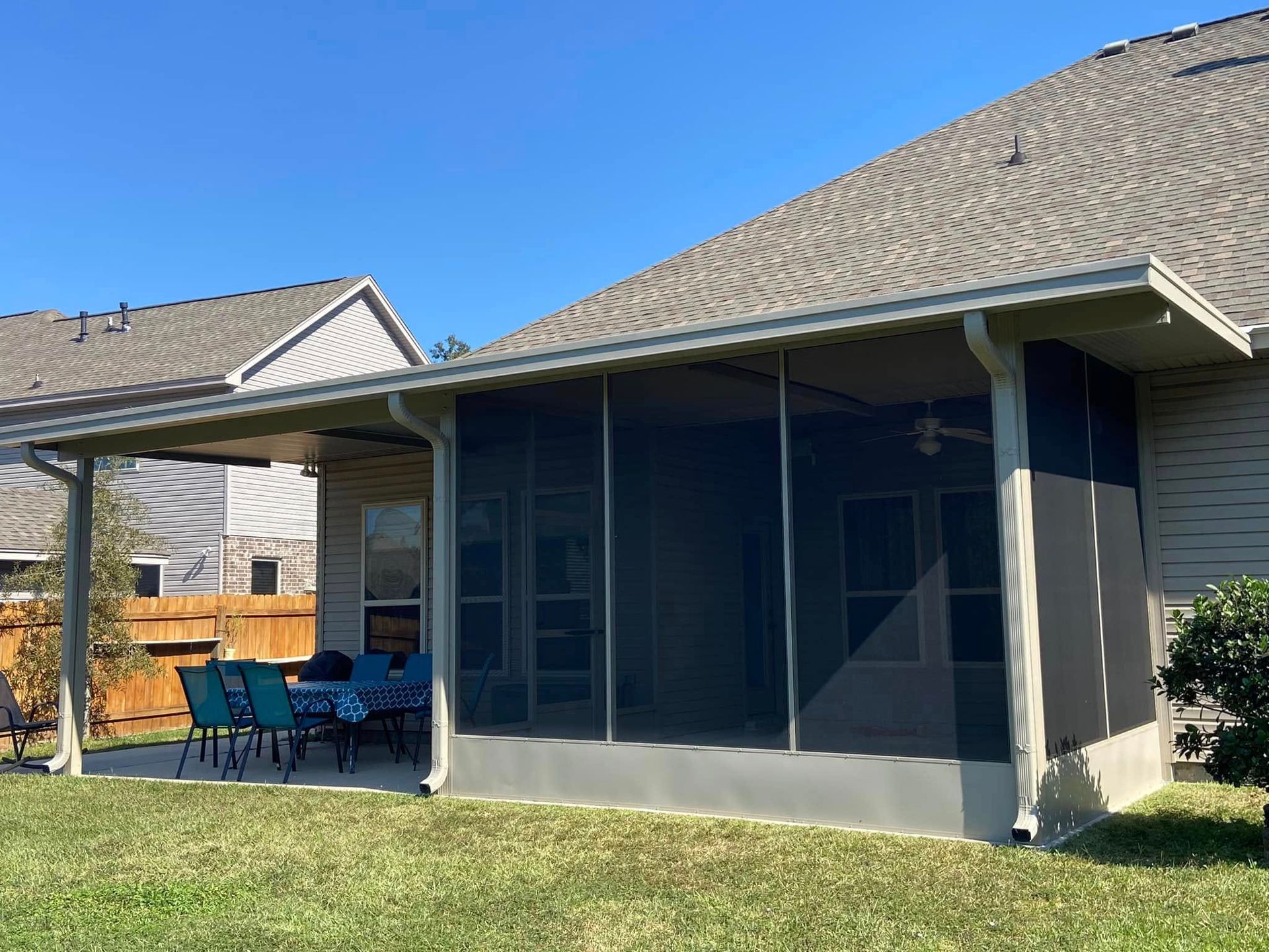 Screened patio attached to a house with a dining table set up and grass in the foreground.