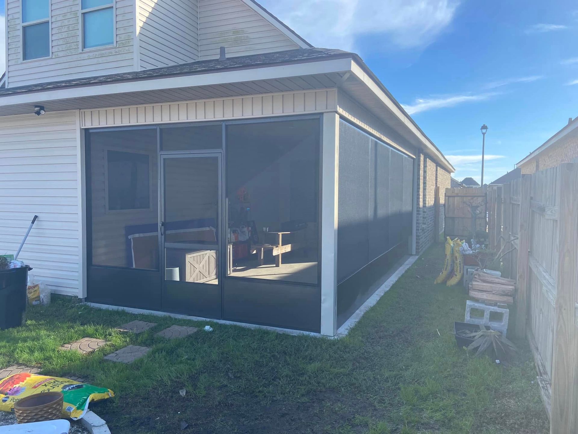 Screened-in porch attached to a house with black screening and white trim, next to a yard and fence.
