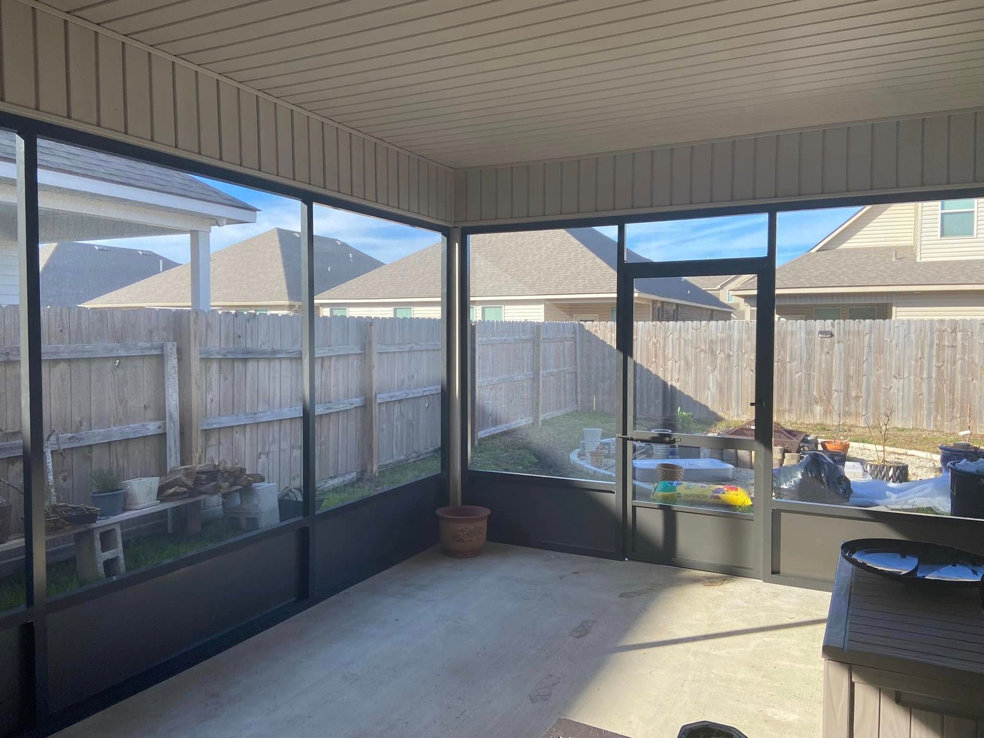 Screened-in porch with dark frames and beige siding. View of backyard and concrete floor, neutral tones.