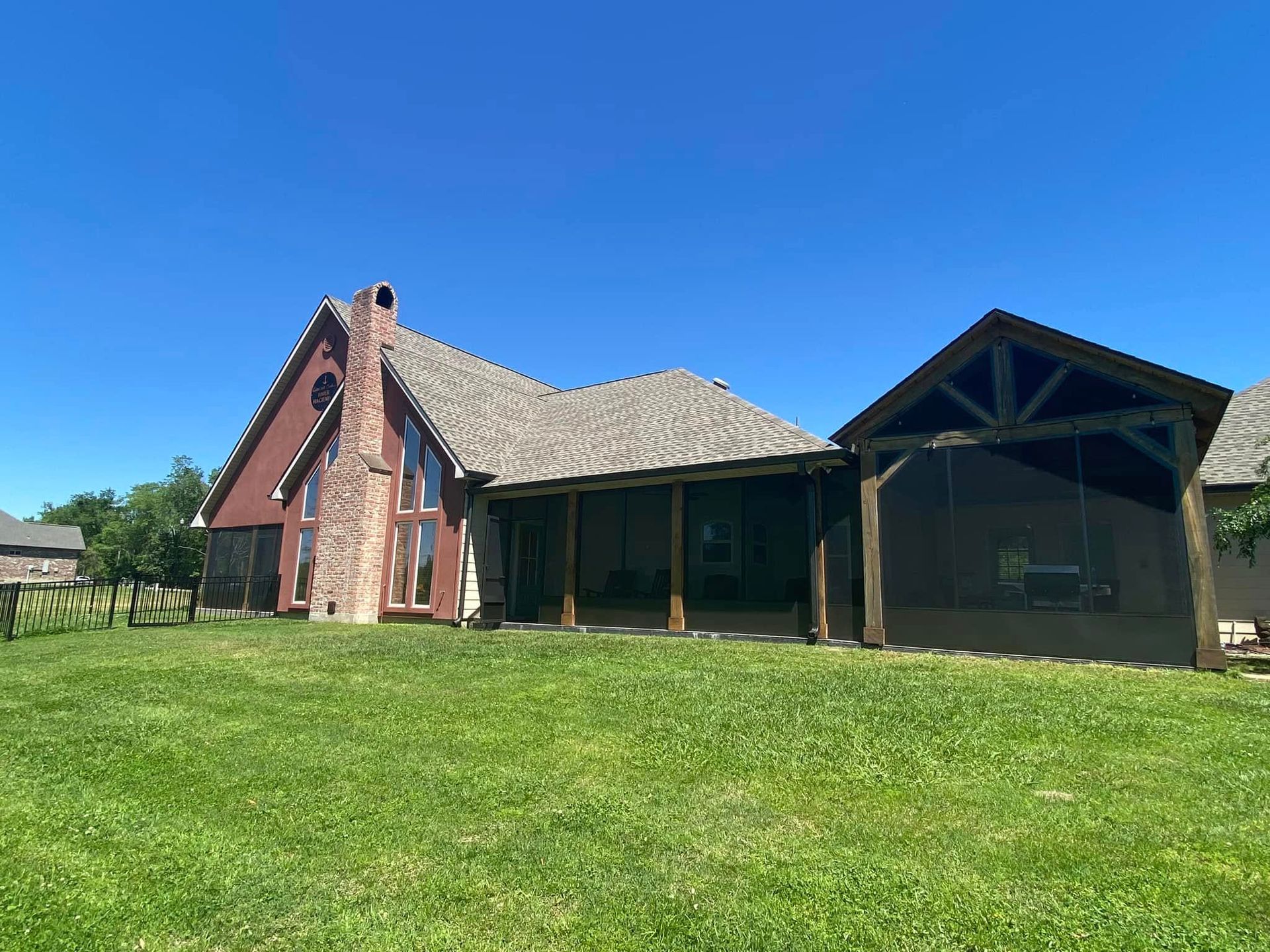 Red house with large windows, a porch, and a swing, on a grassy lawn under a clear blue sky.