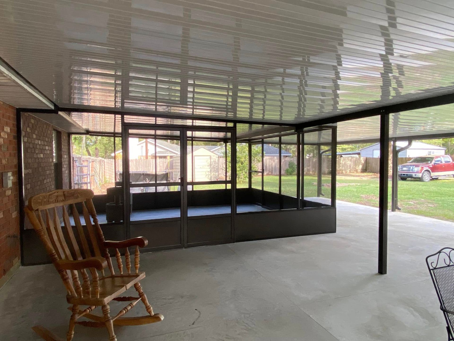 Outdoor patio with a screened-in enclosure. A rocking chair sits on the patio; green yard visible.