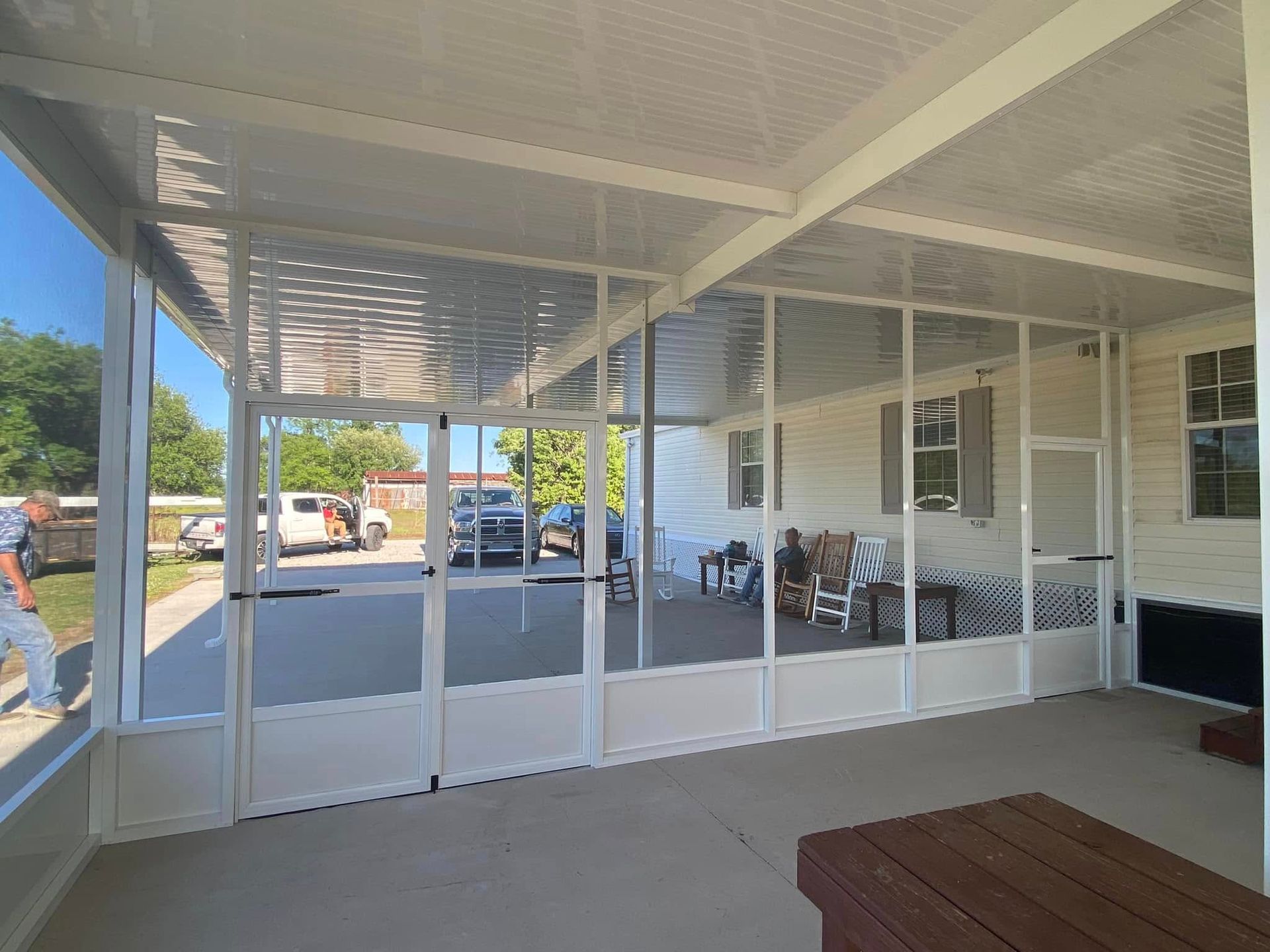 A screened-in patio attached to a light-colored house, with white frames, and a concrete floor.