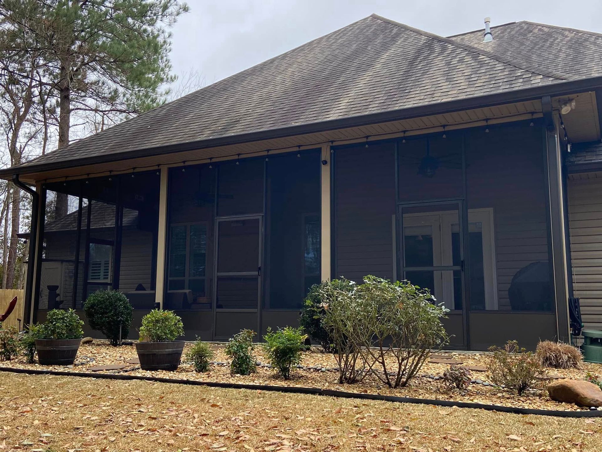Screened-in porch with potted plants and a brown roof. Lawn in front, overcast sky.