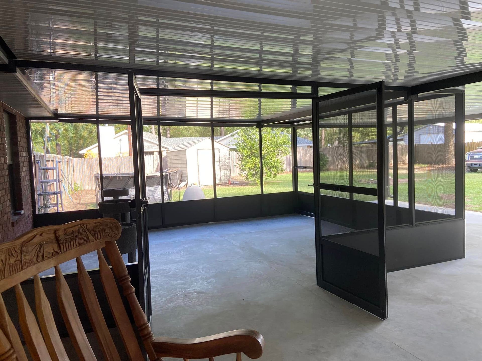 Screened-in porch with black frames, clear panels, and a wooden rocking chair. Exterior view of backyard.