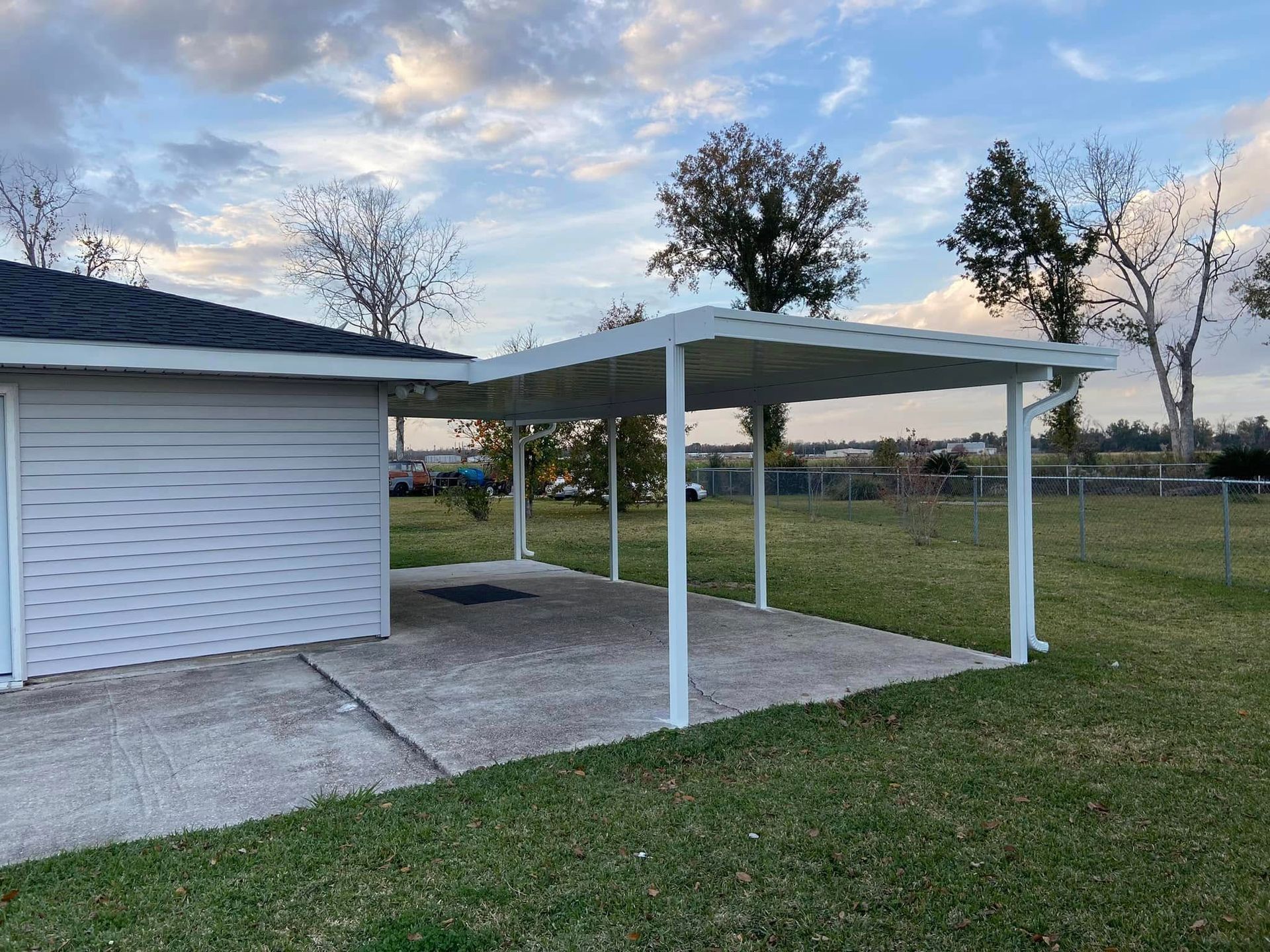 White carport attached to a house, covering a concrete patio, in a grassy yard.