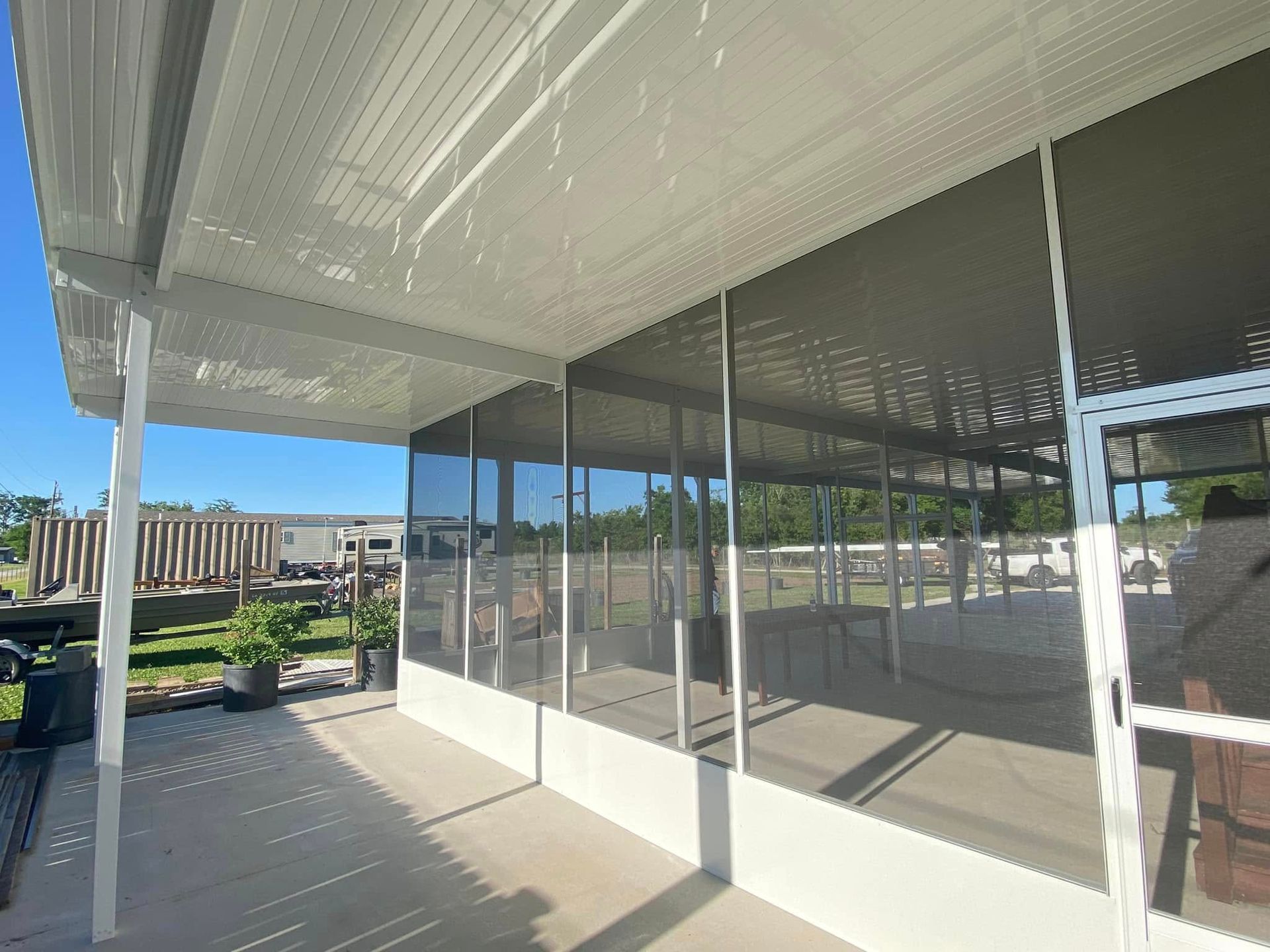 Screened patio with white frame and roof. Sunshine reflecting on the concrete floor.