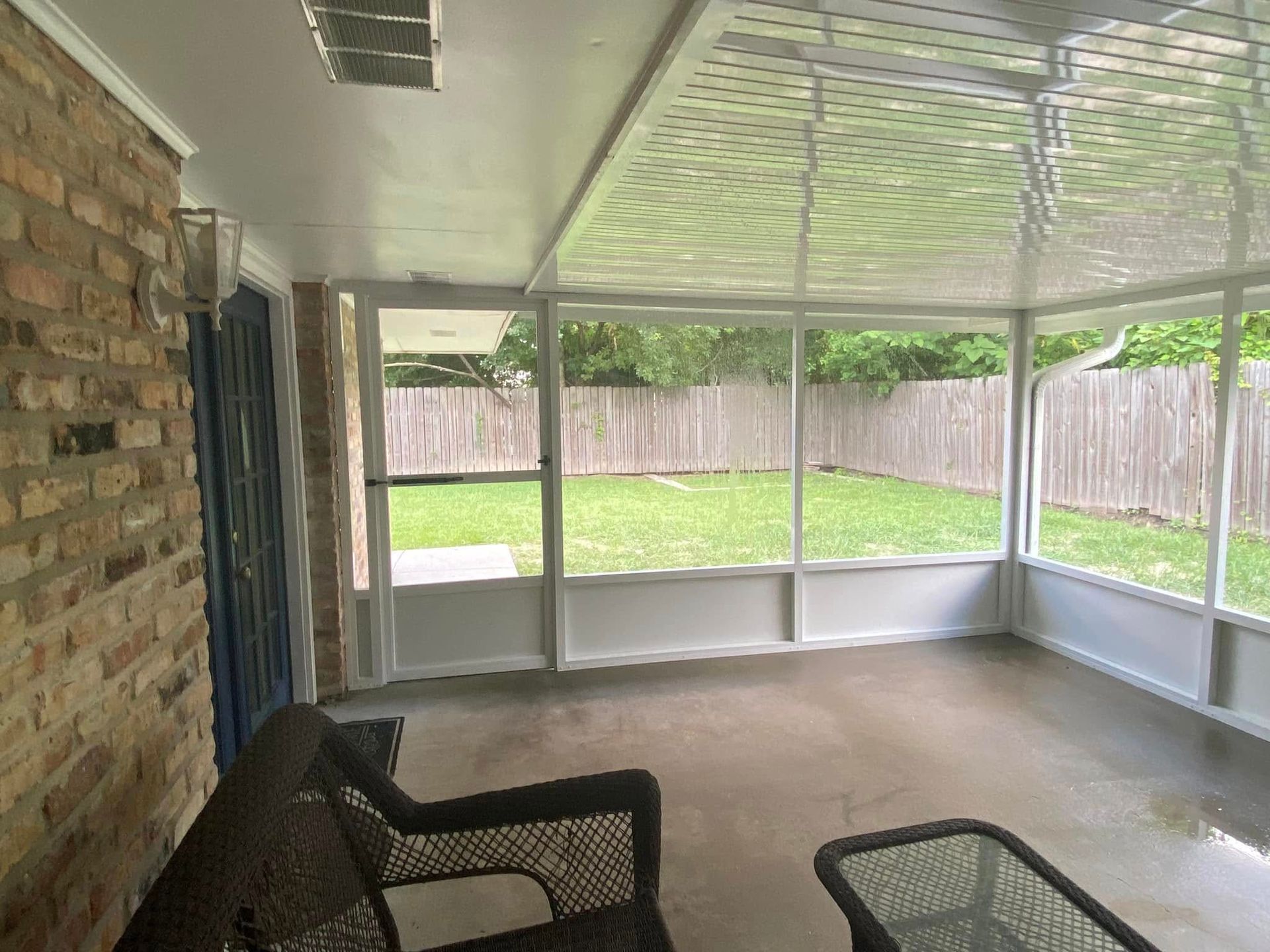 Sunroom with wicker furniture, brick wall, and a view of a grassy backyard.