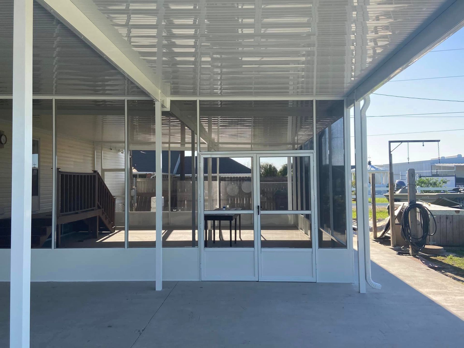 White screened porch with door, built on a concrete patio, beside a house.