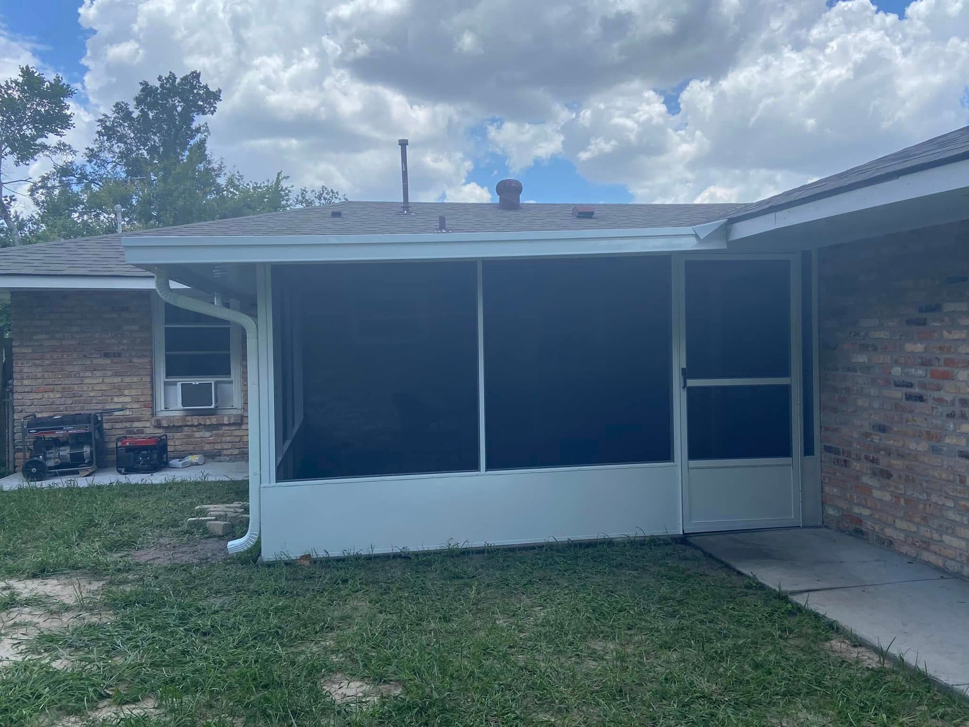 Screened porch with white frame attached to a brick house under a cloudy sky.