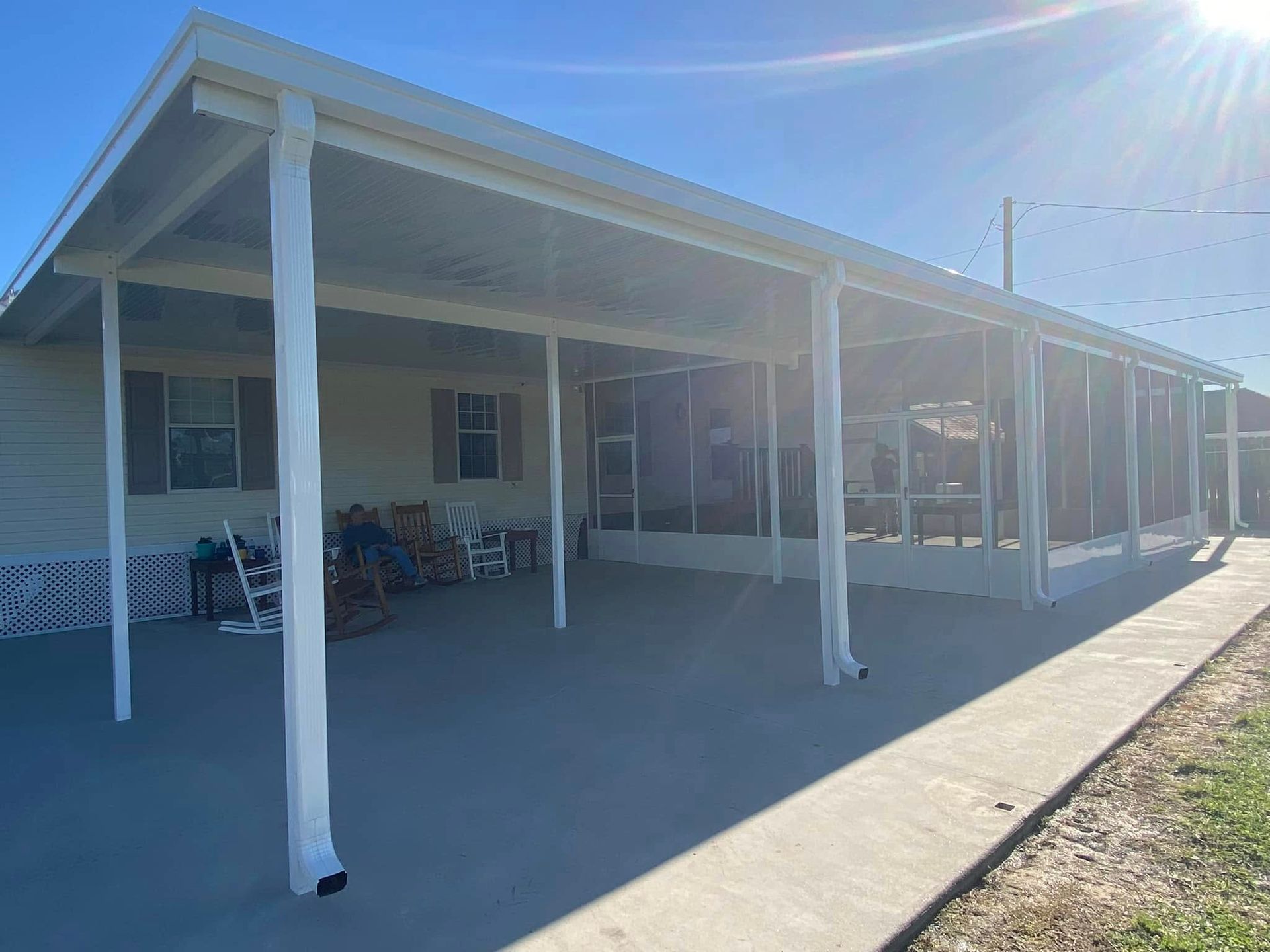 White screened-in porch attached to a light-colored house with concrete path on a sunny day.