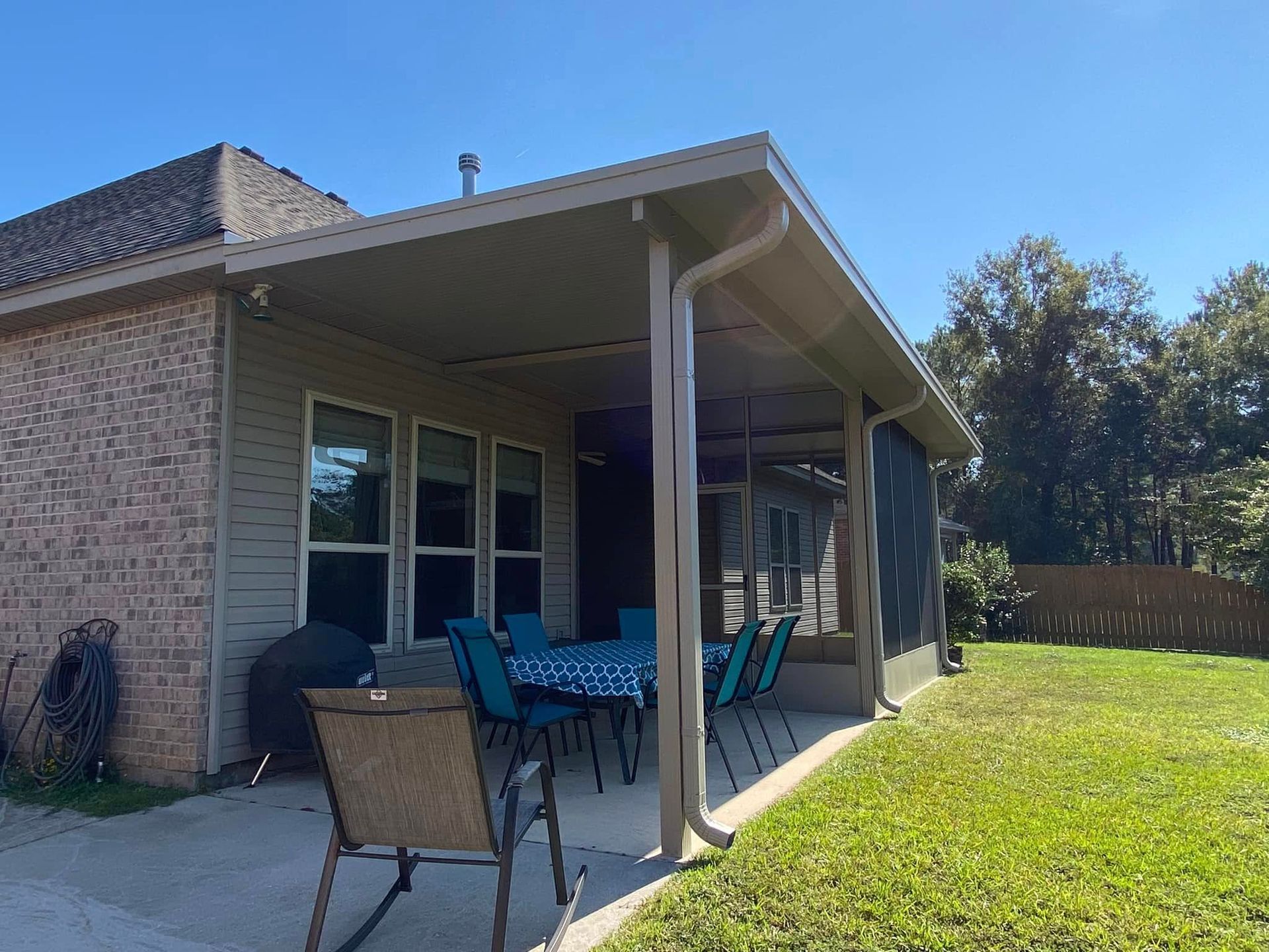 Patio with screen enclosure, table, chairs, and a house with brick and green siding.