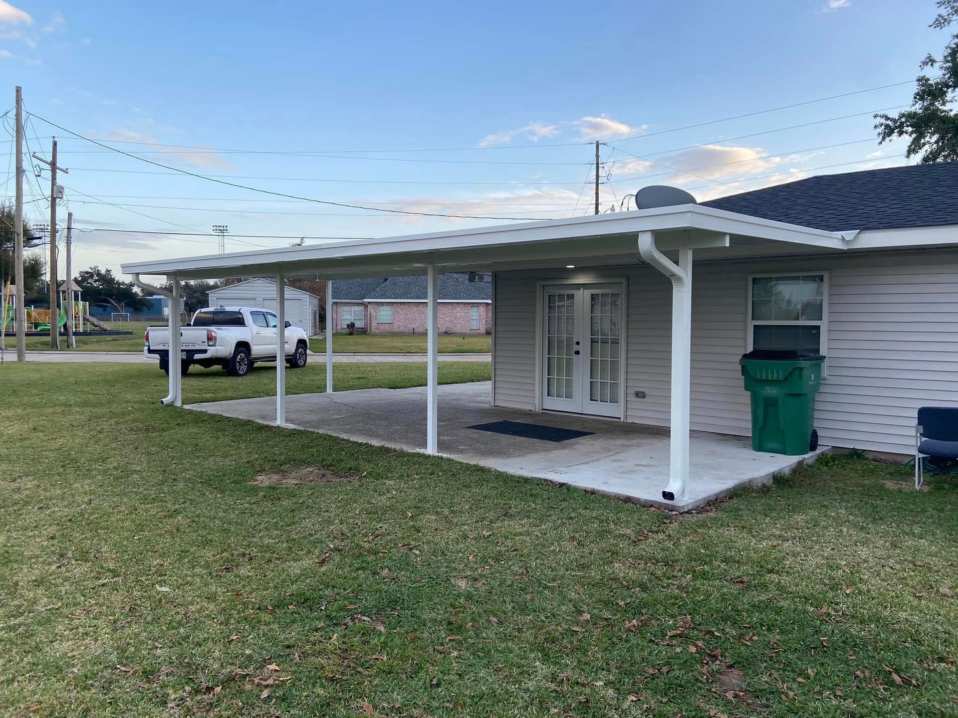 Backyard patio with white awning, concrete slab, green trash can, and white truck.