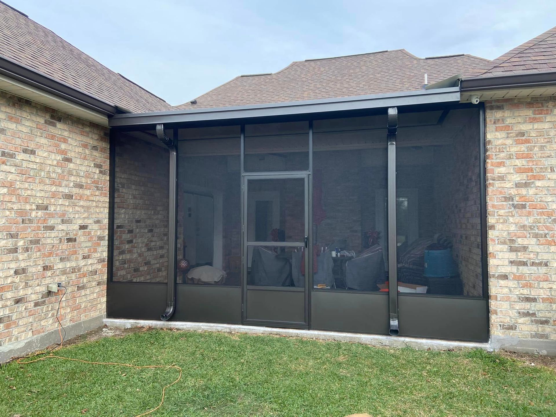 Screened-in patio with dark frames against brick walls, door in center, situated between a home's exterior walls.