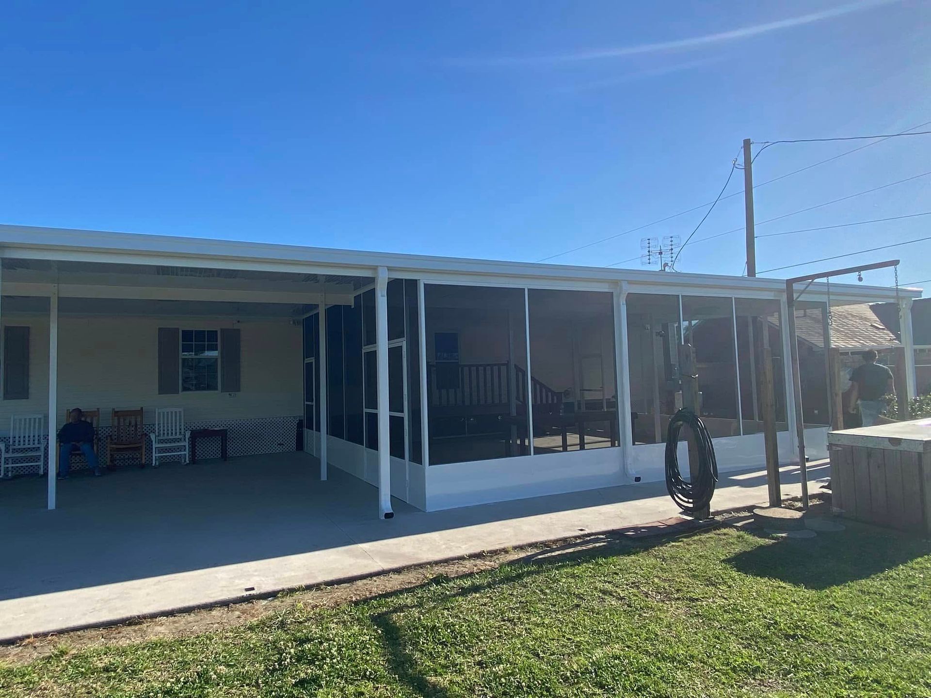 Screened porch attached to a tan home on a sunny day. Green grass and blue sky are visible.