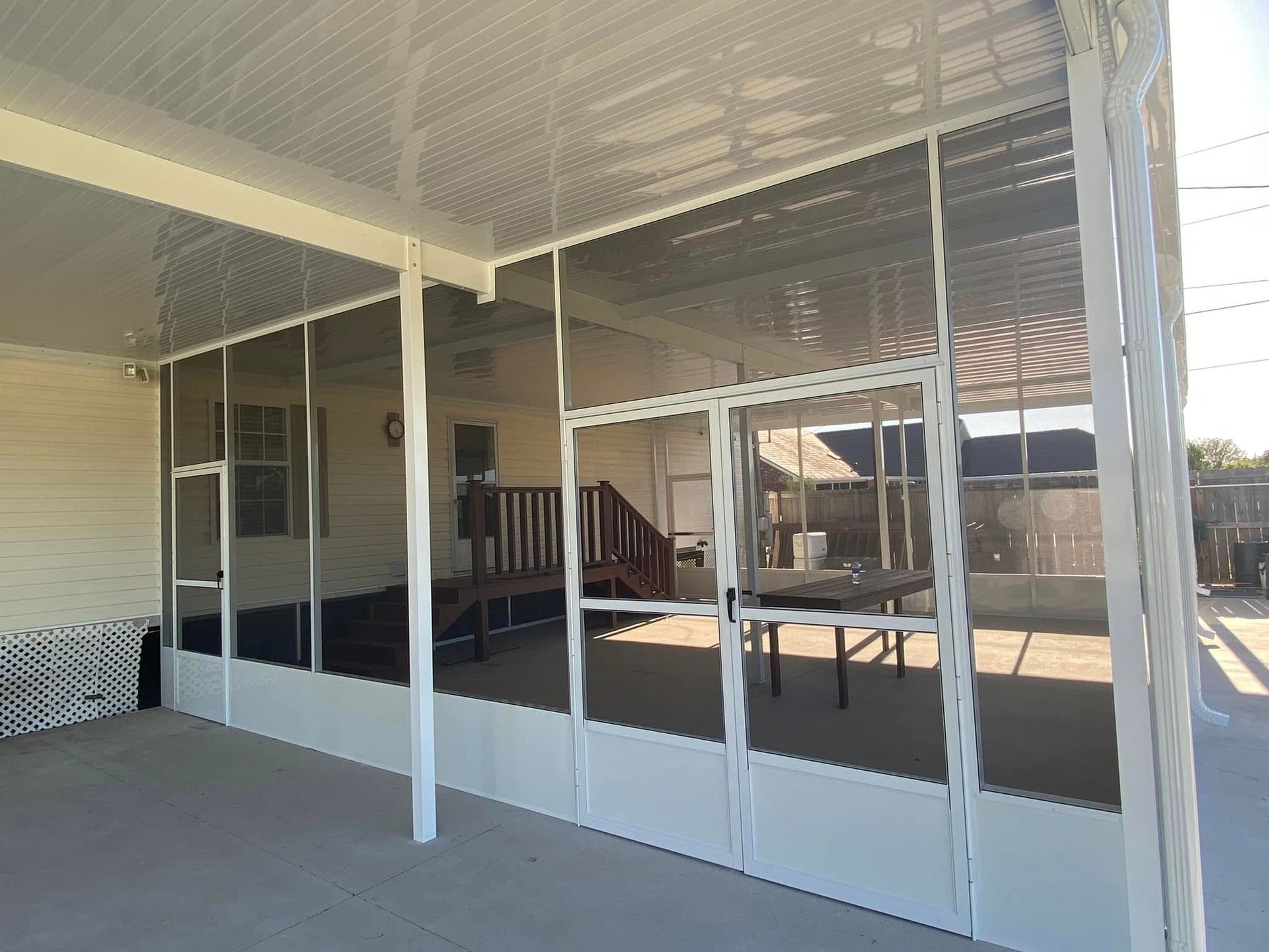 Screened-in porch with white frame, clear roof, and door, attached to a yellow house.