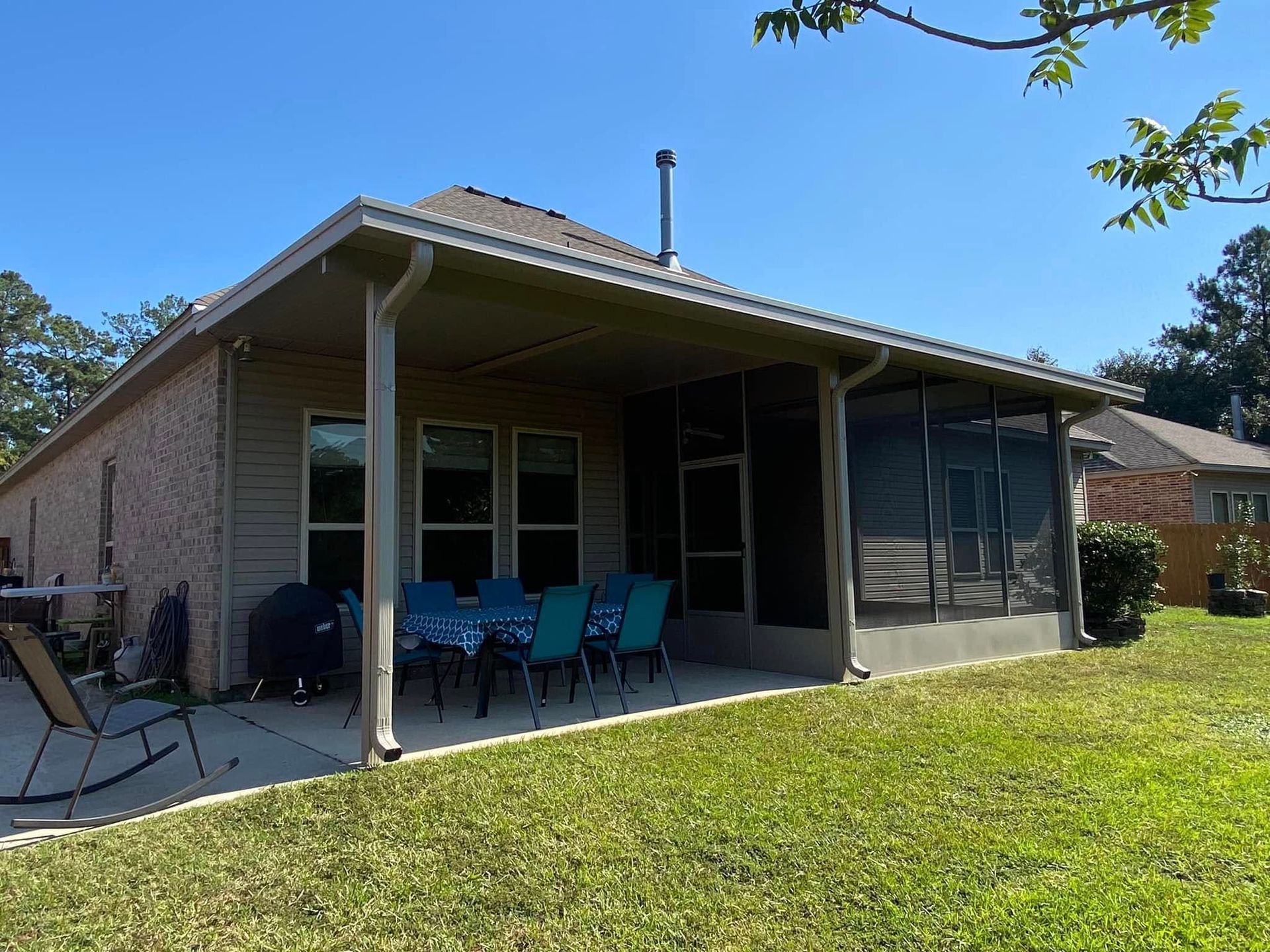 A brick and siding house with a screened patio, dining set, and green lawn under a blue sky.