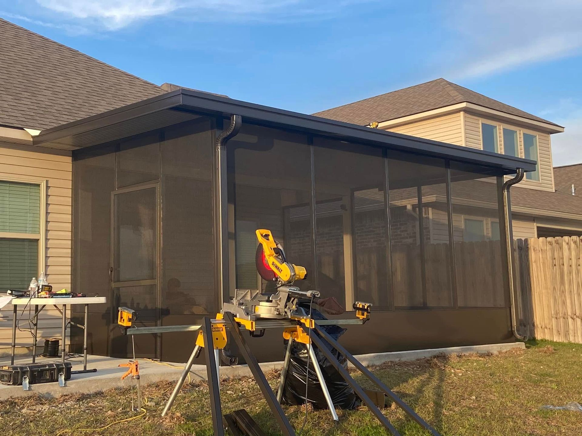 A partially built screened-in porch with a miter saw, next to a house and backyard.