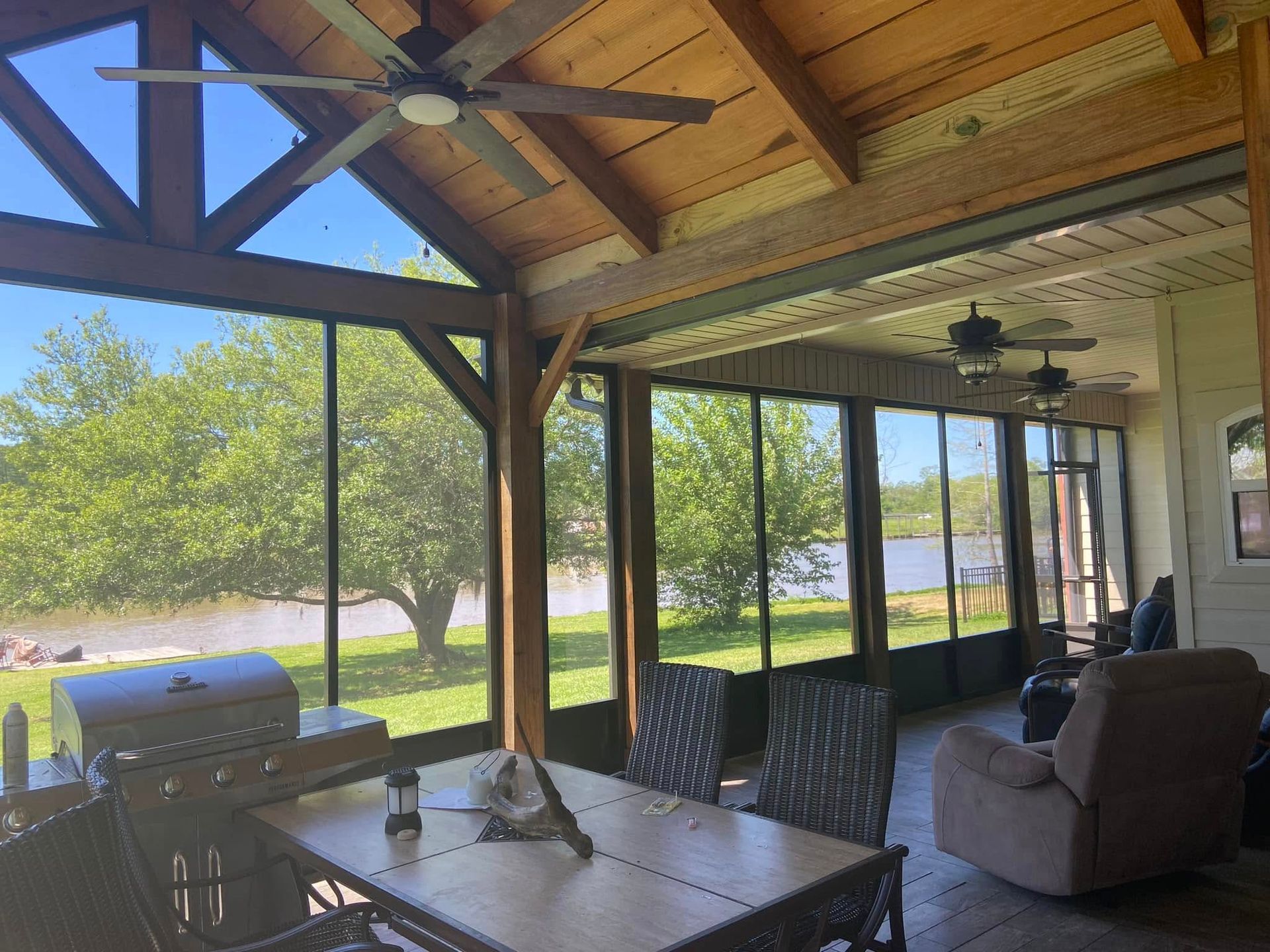 Screened porch with lake view, dining table, grill, wicker chairs, and recliner. Ceiling fans.