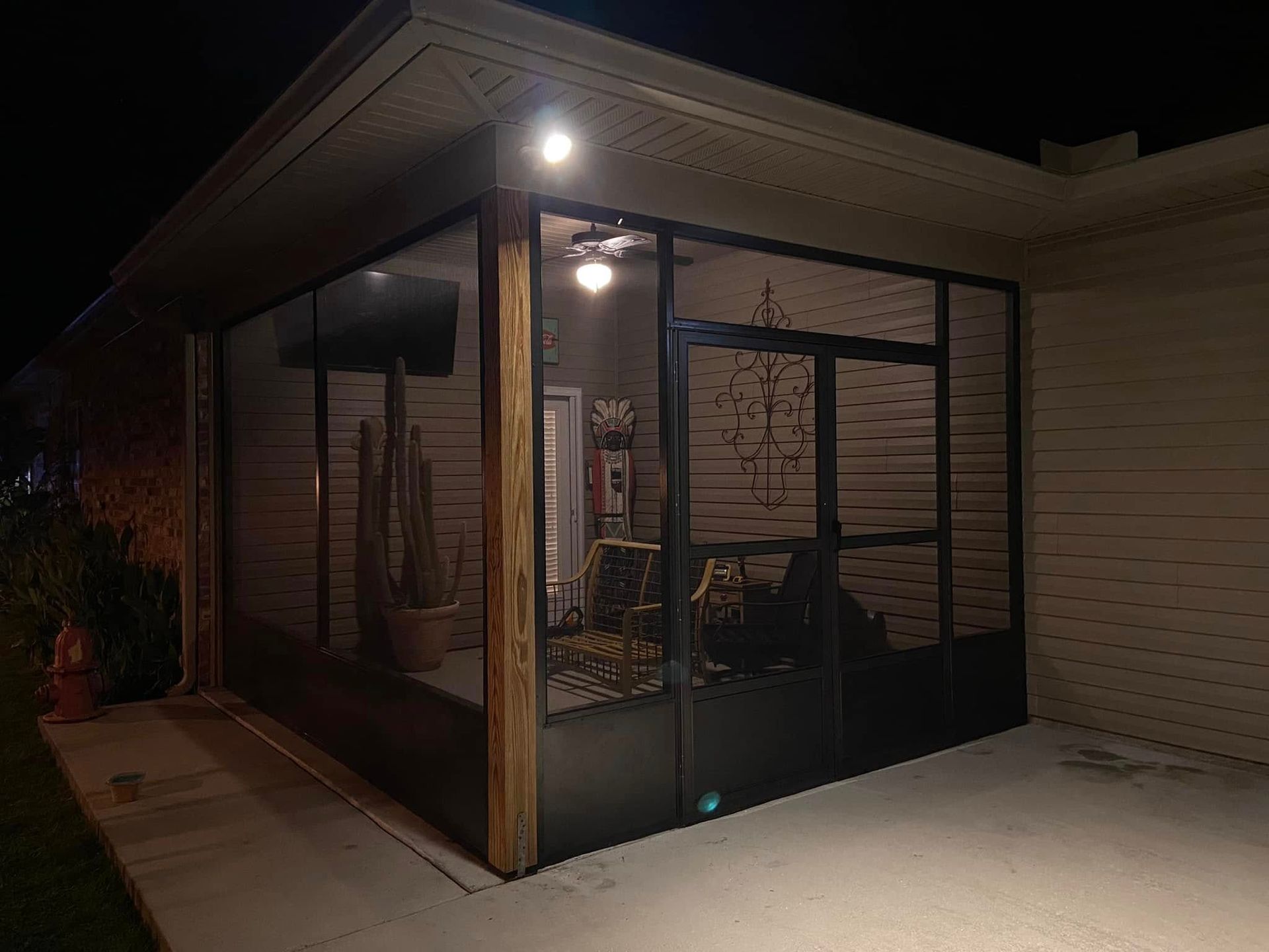 Screened-in porch lit at night. Dark screens with outdoor furniture and potted plants.