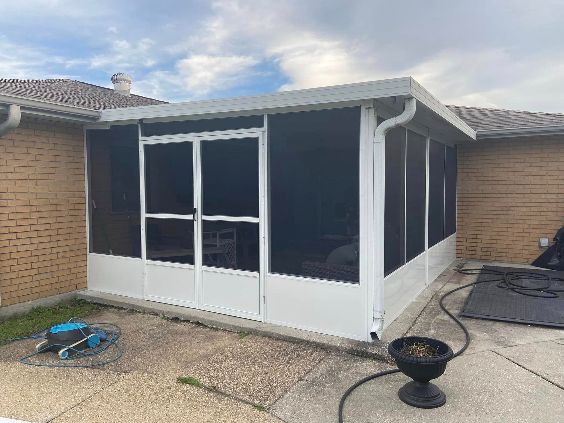 Screened-in porch attached to a brick house, white frame, black screens, a door, and a concrete patio.