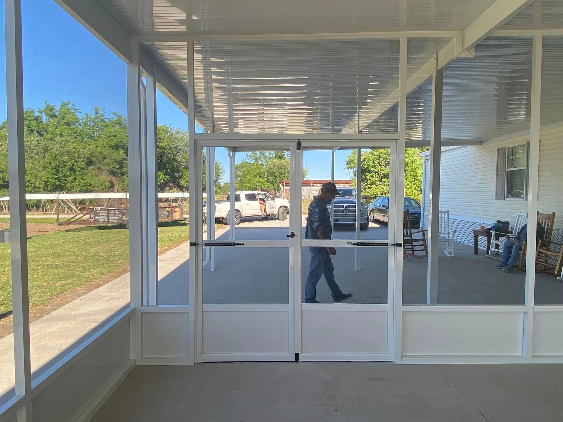 A screened porch with glass doors leading to a paved area where a person walks.