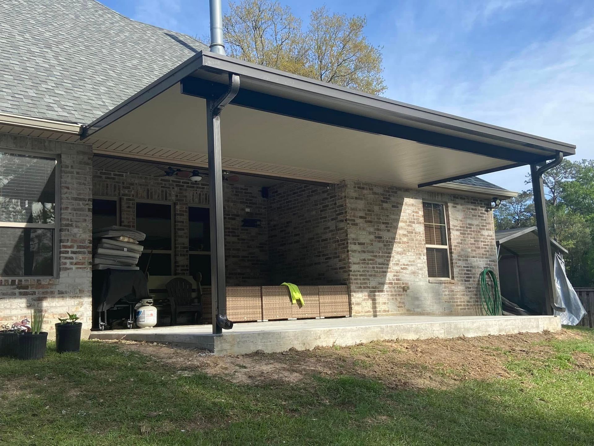 Patio with brick wall and gray roof, black support beams, and flat white ceiling.