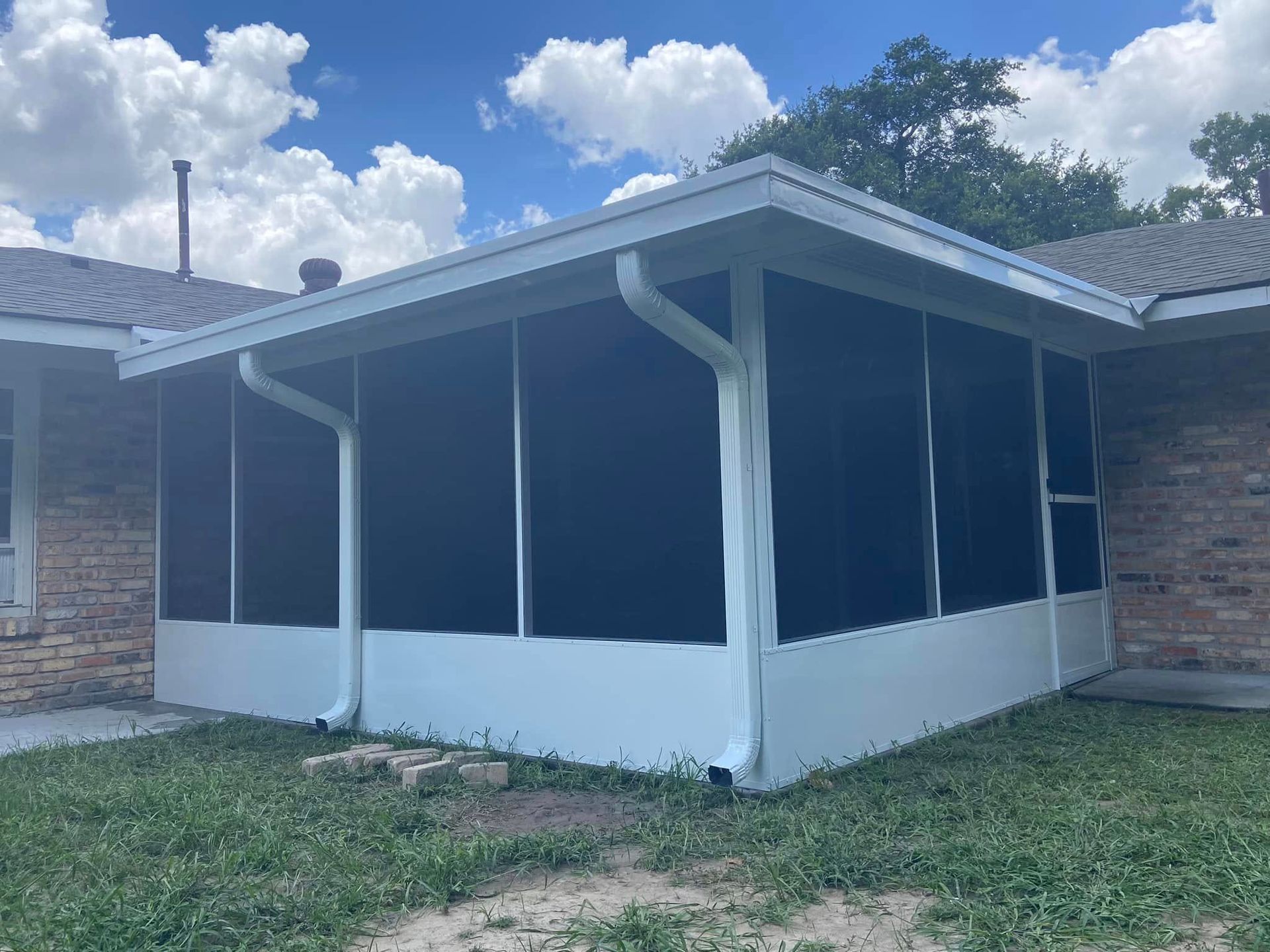 White screened-in porch attached to a brick house with a blue sky and clouds.