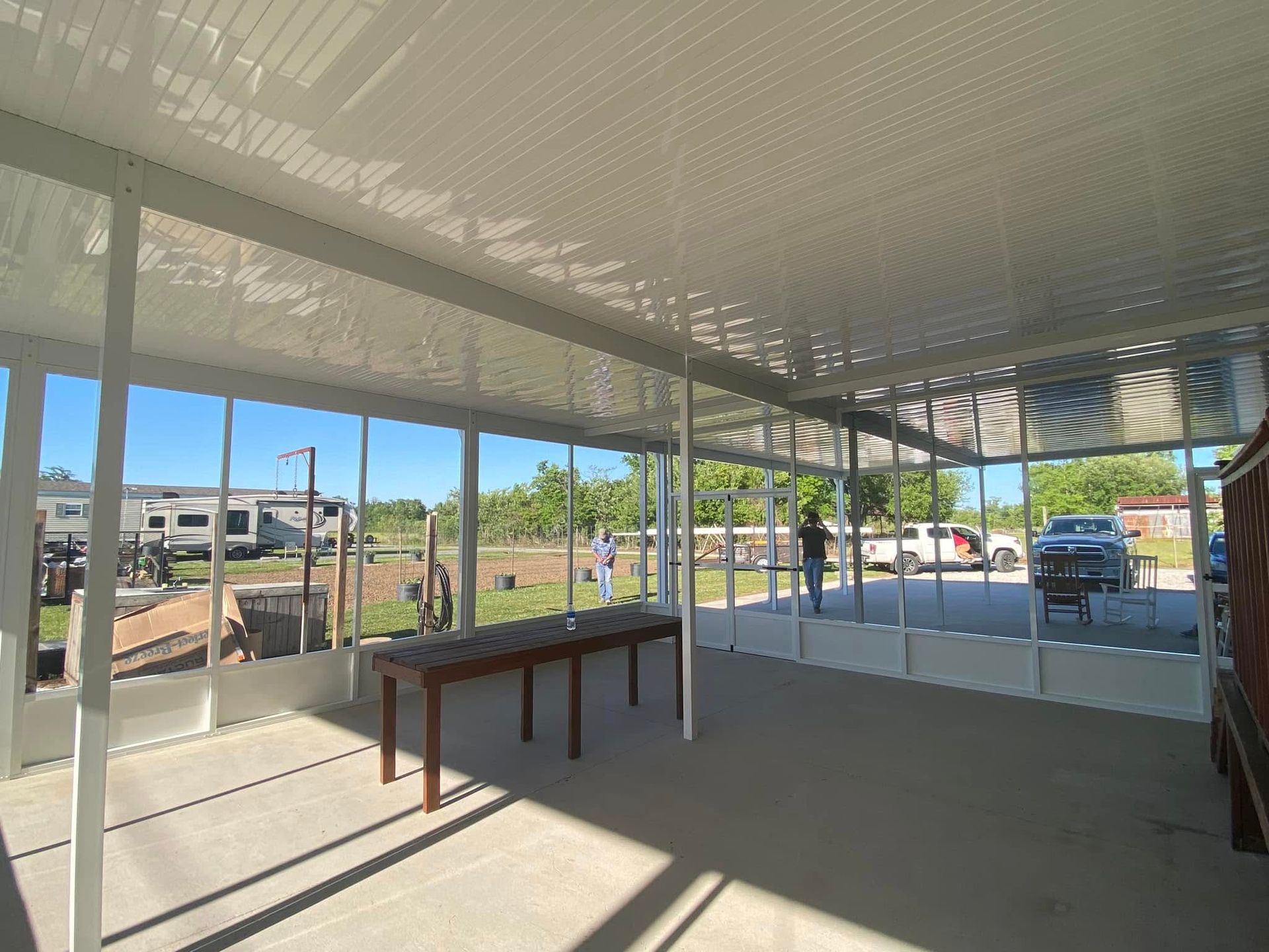 White-framed screened porch with a view of a yard and RVs. Sunlight streams in.