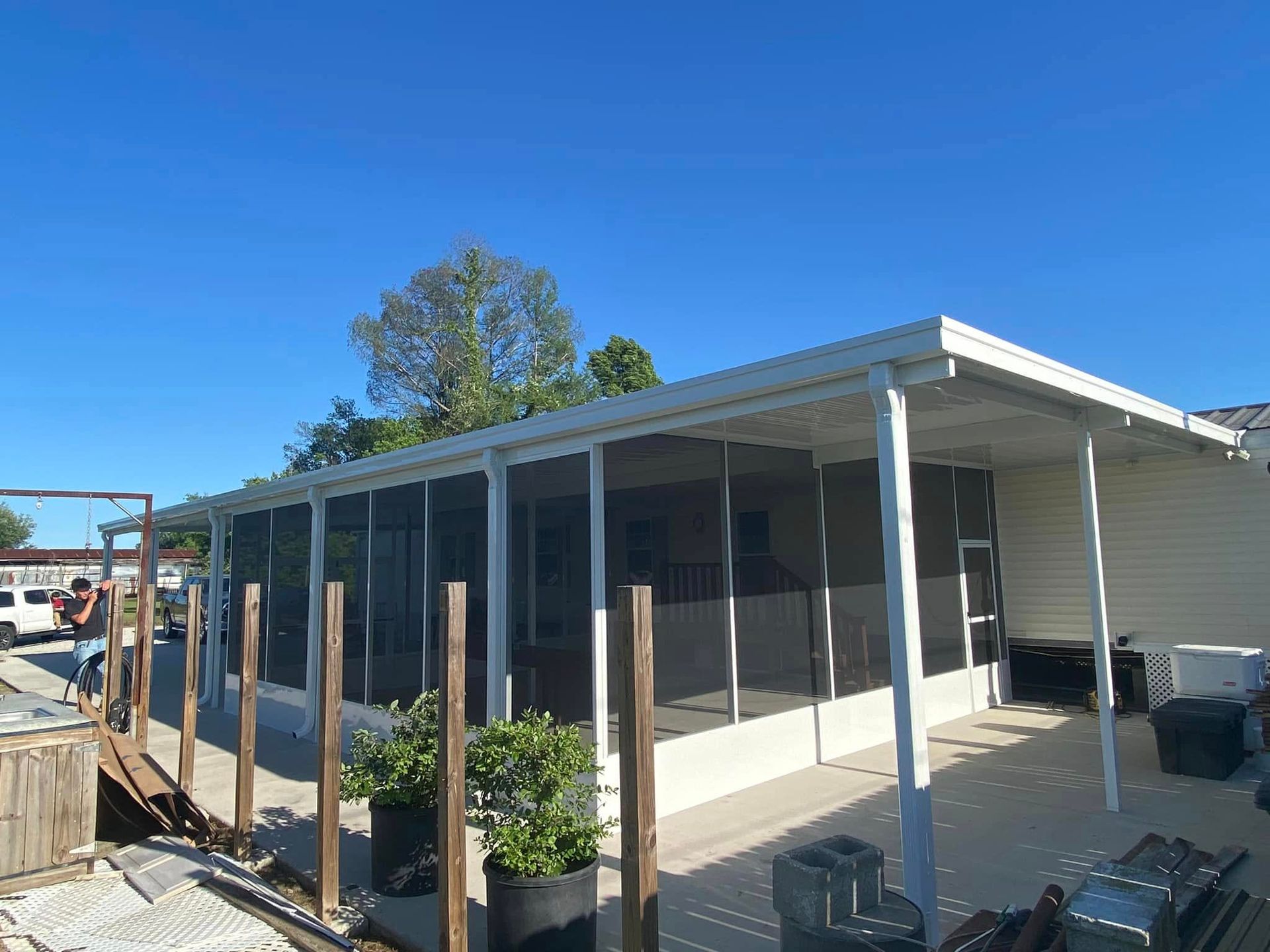 White screened porch with white supports, against a blue sky. Person works near wood fence.