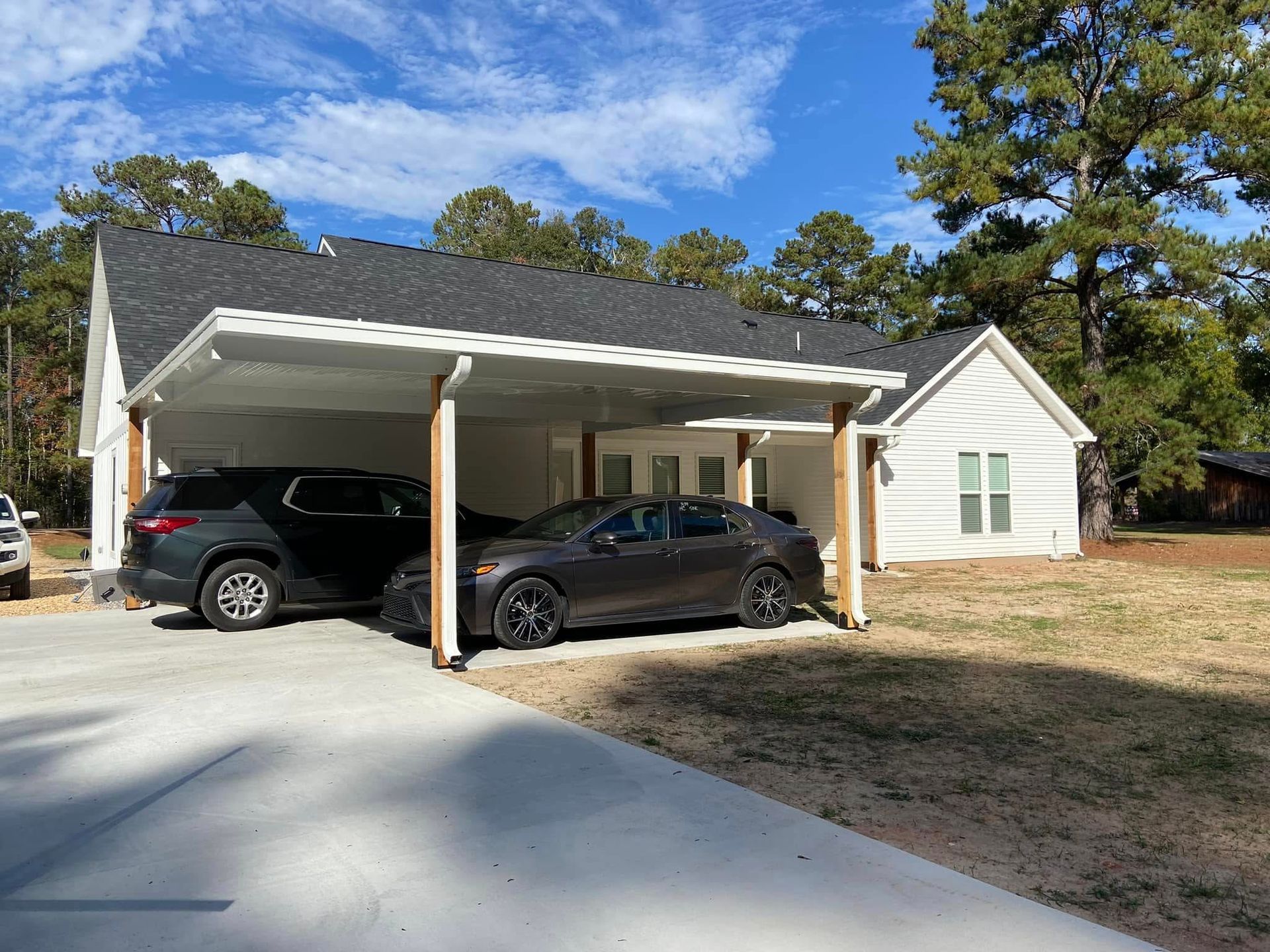 Cars parked under a white carport attached to a white house, on a sunny day.
