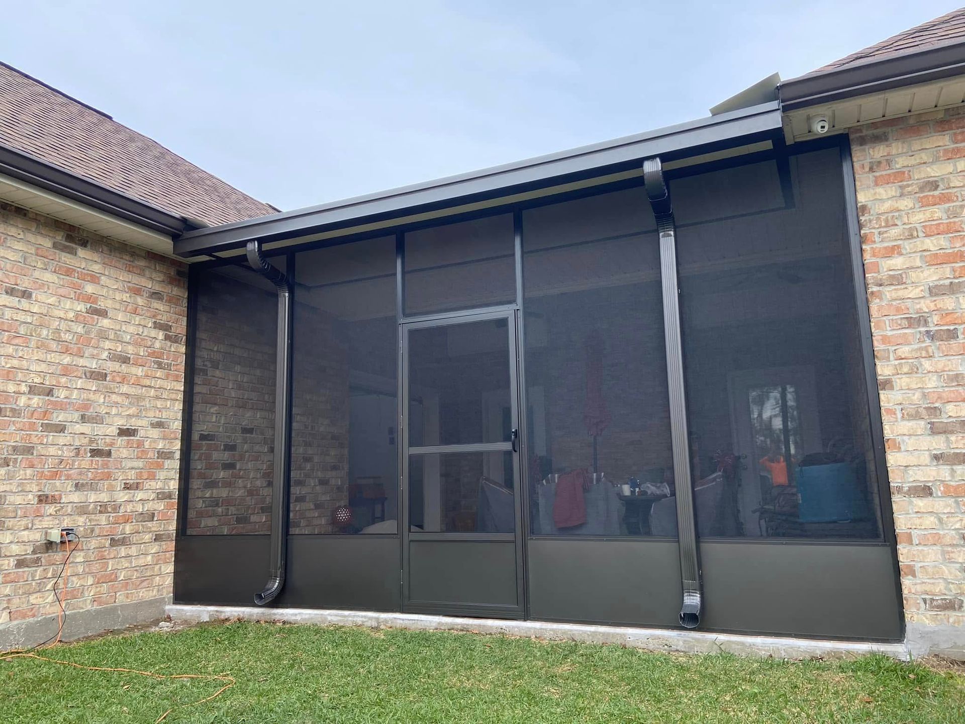 Screened-in porch with black framing, attached to a brick house. Green grass in front.